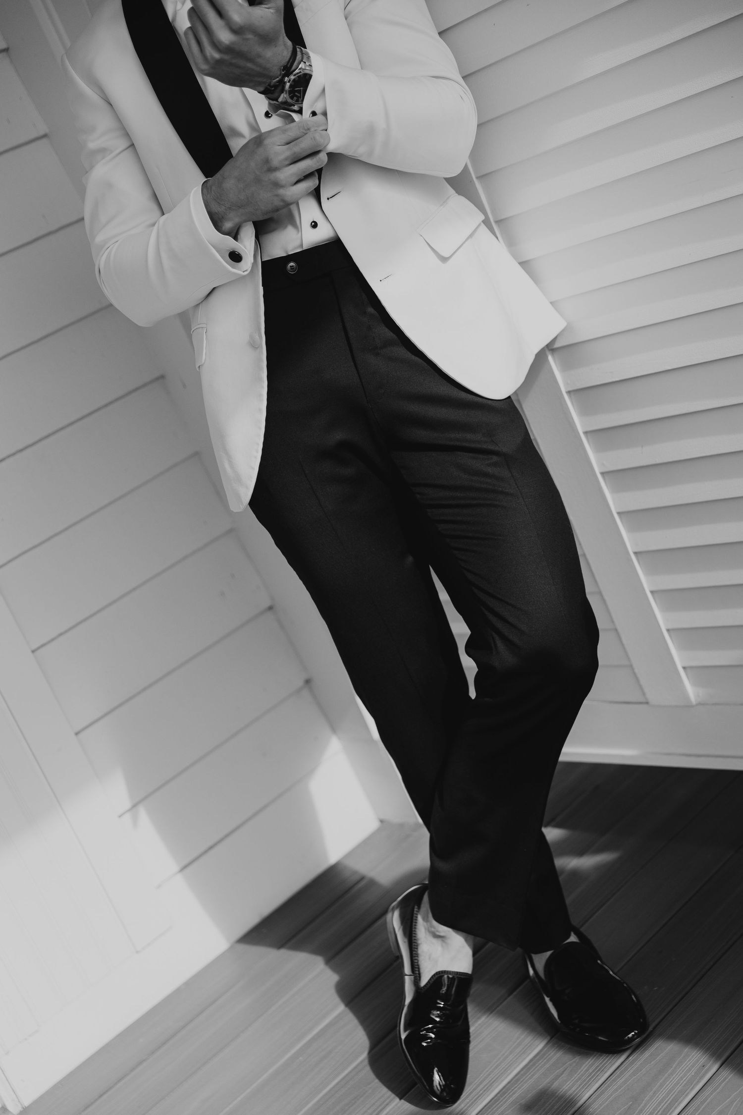 Black and white photo of a formal outfit featuring a white blazer, dark trousers and patent leather dress shoes.