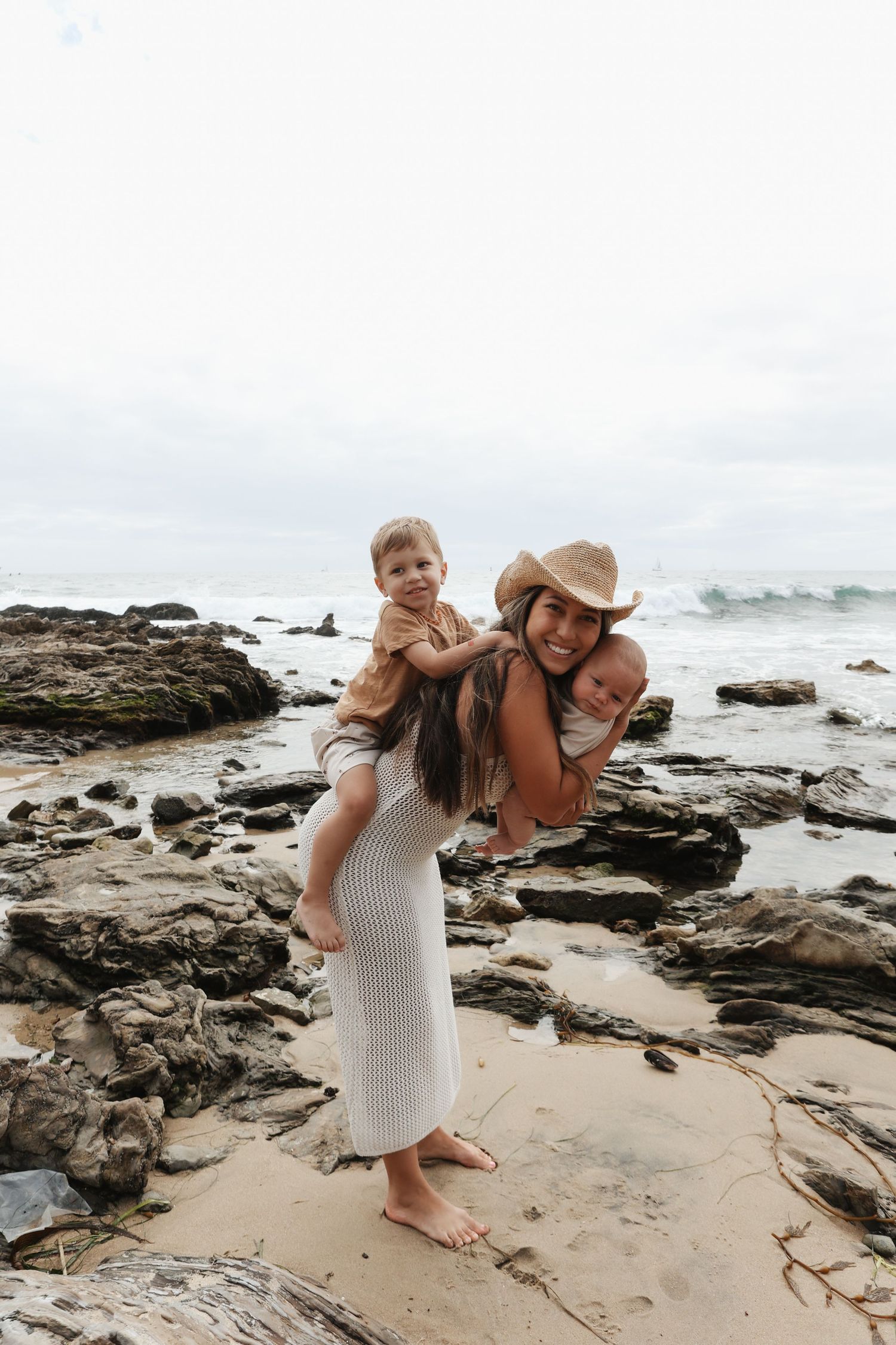 Mother and child playing together on a rocky beach shoreline during a cloudy day at the ocean.