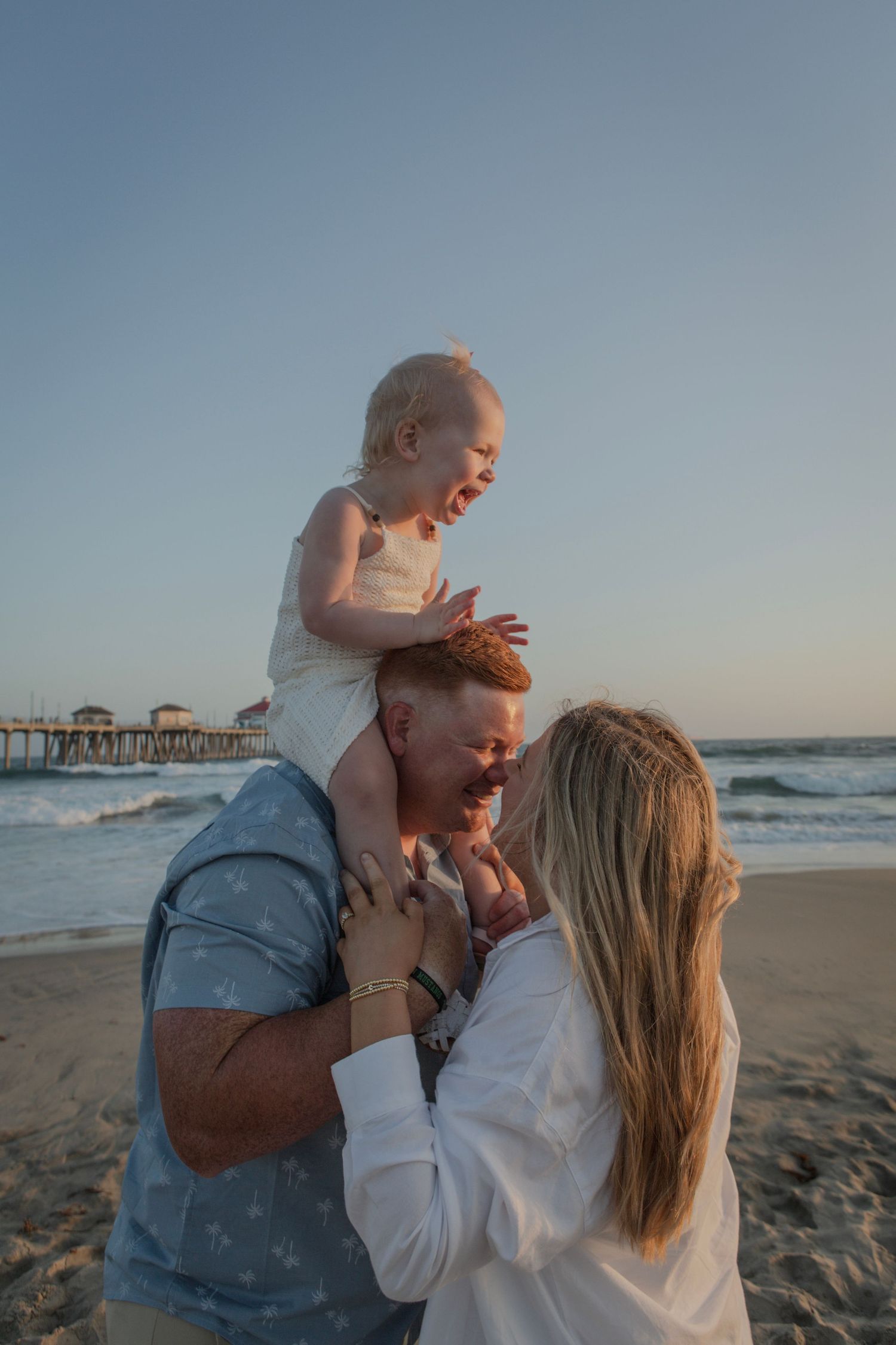 A tender family moment shared on a beach with a pier in the background.