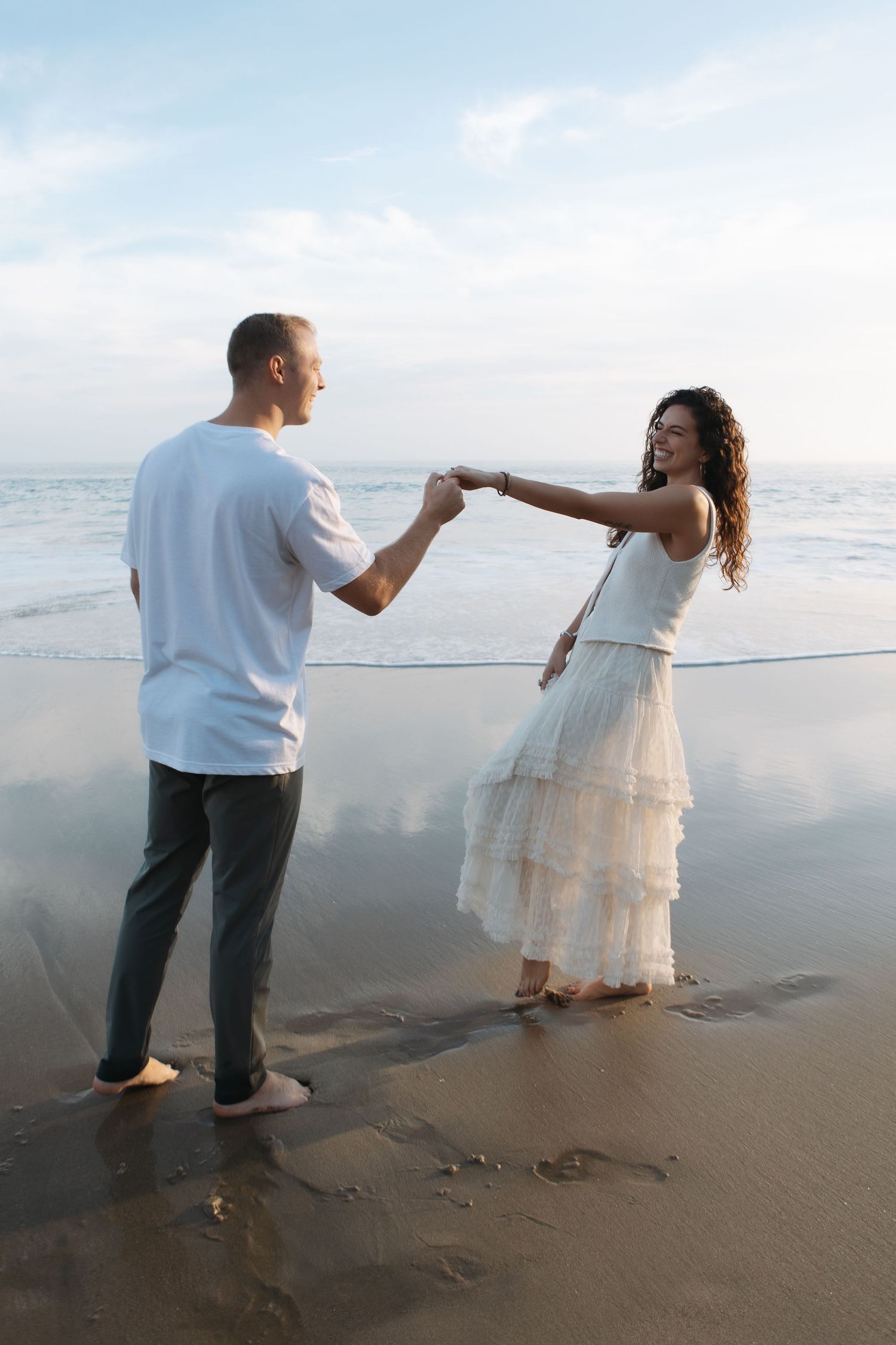 A couple dances together on a misty beach at sunset, creating a romantic silhouette against the ocean backdrop.