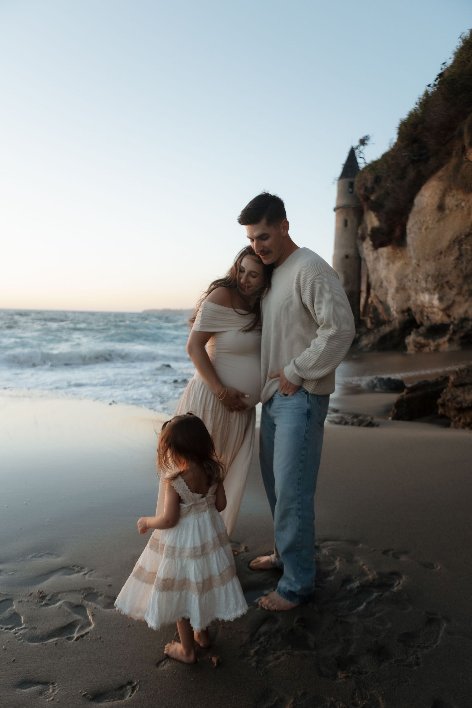 A family shares tender moments together on a misty beach at sunset near dramatic coastal cliffs.