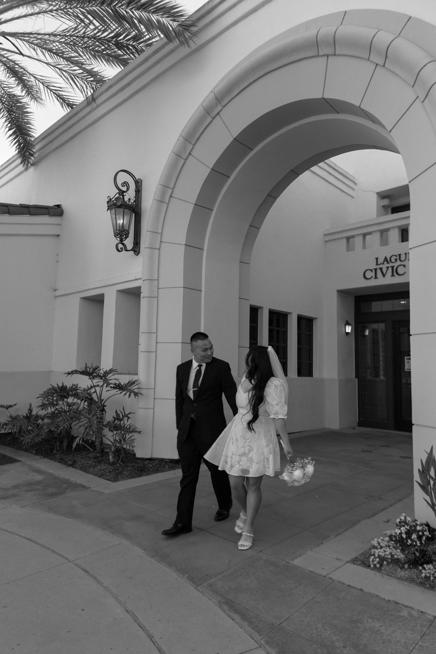 A couple exits the Laguna Civic building under an arched entryway in black and white.