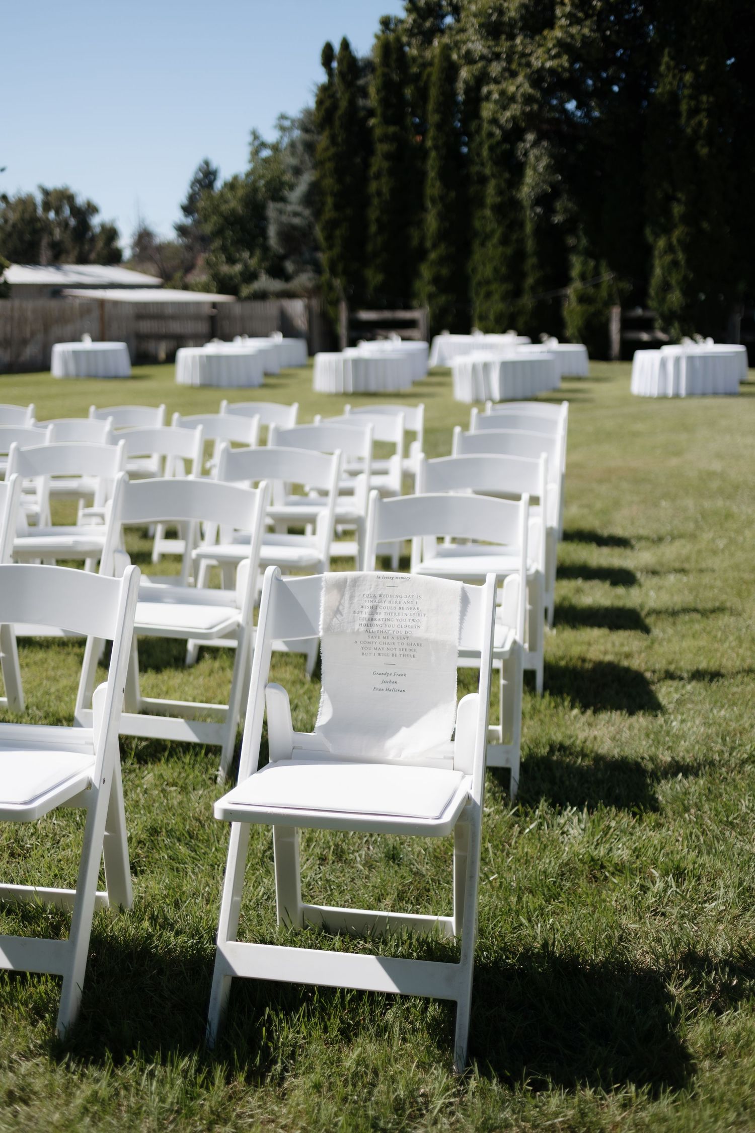 White folding chairs arranged on grass for an outdoor memorial service with name cards attached to each seat.
