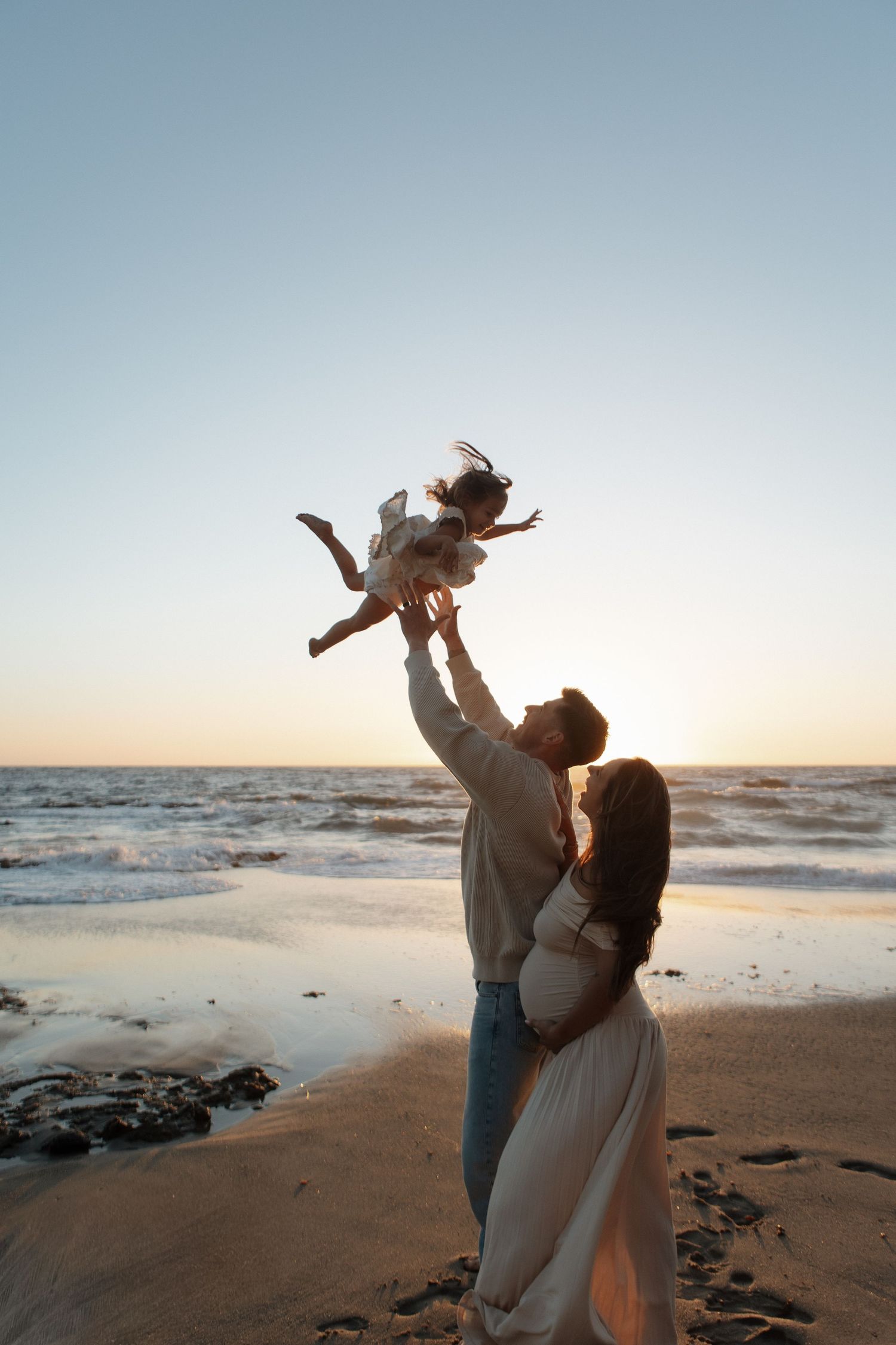 A couple shares tender moments on a beach at sunset while holding their baby up in a series of connected photos.