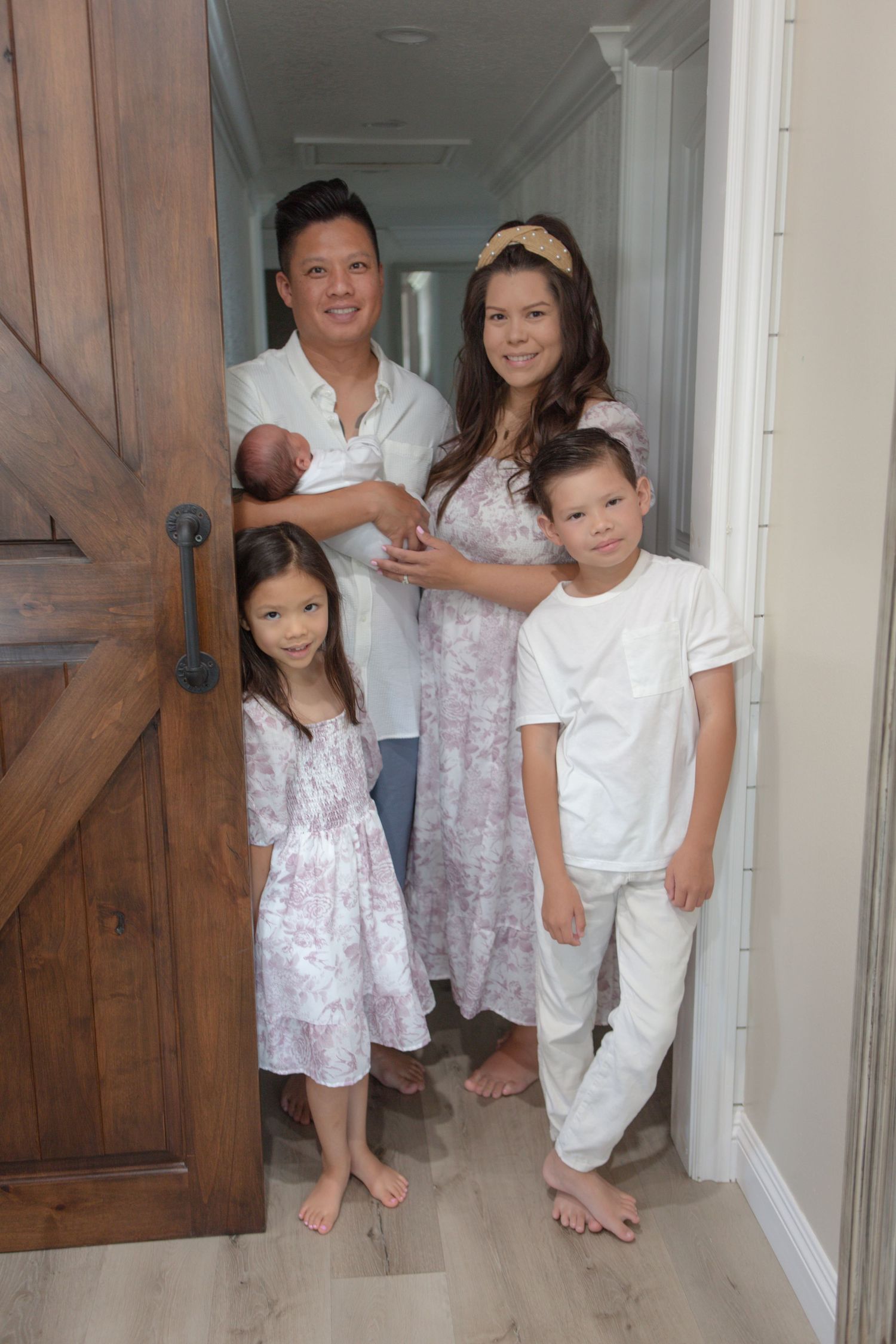 A family of five poses together in a white hallway with a rustic wooden door.