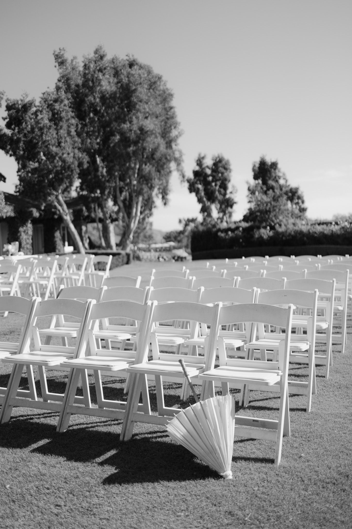 Black and white photo of white wedding ceremony chairs arranged on a lawn.