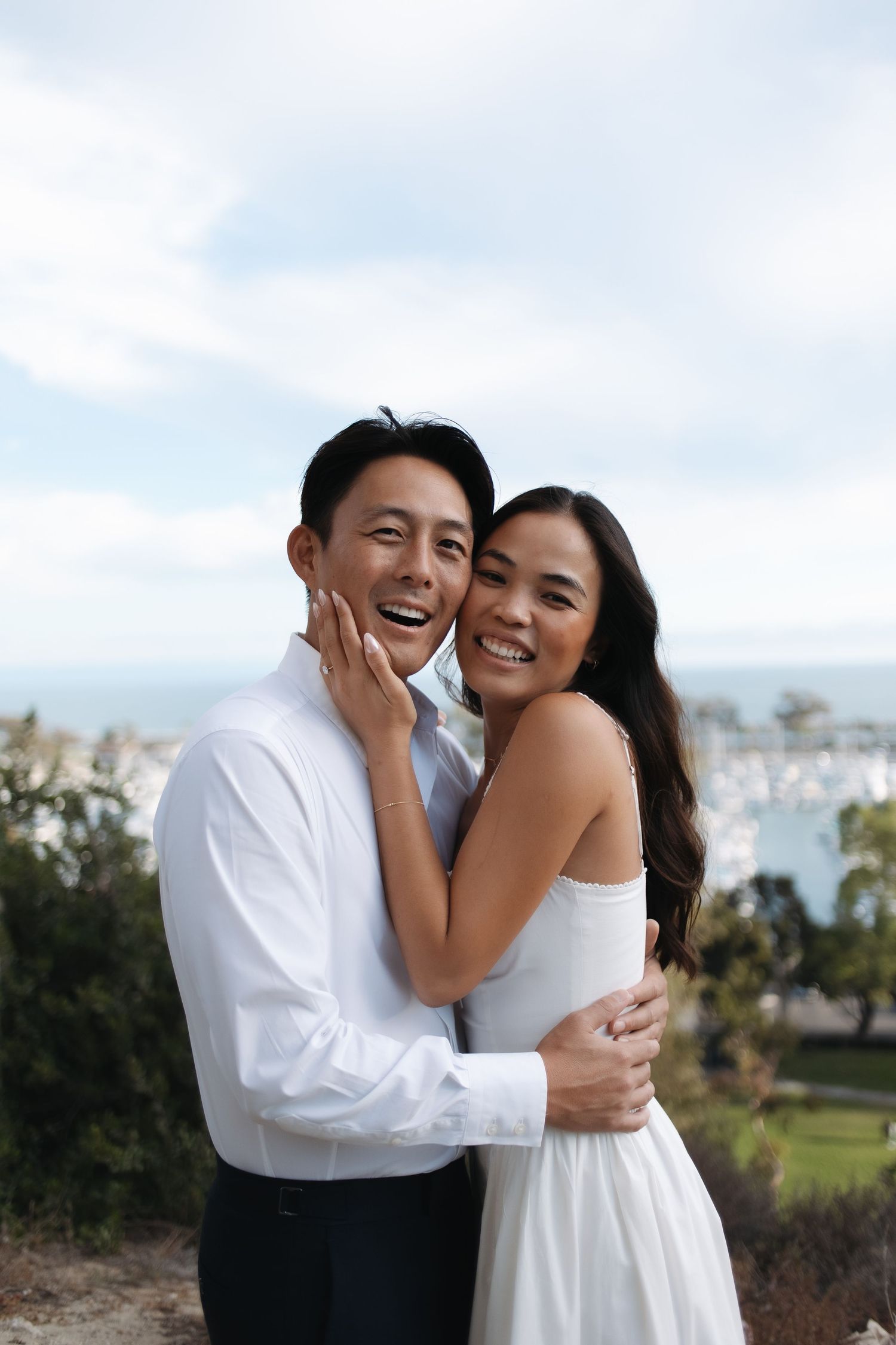 A couple in white embraces and laughs joyfully together during an outdoor photo session.