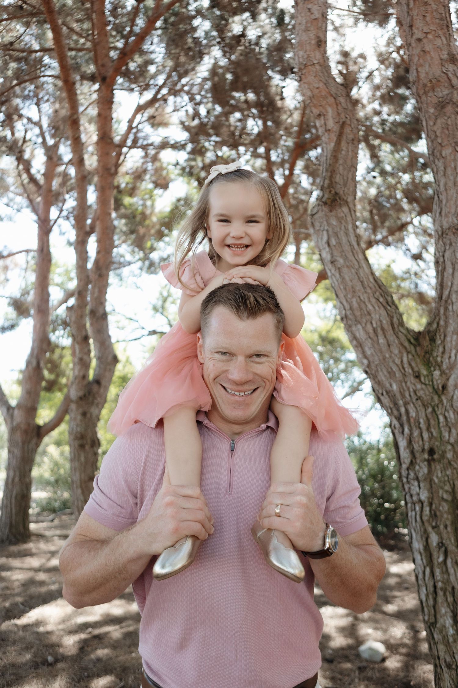 Parent and child playing together outdoors in a wooded area wearing matching pink shirts.