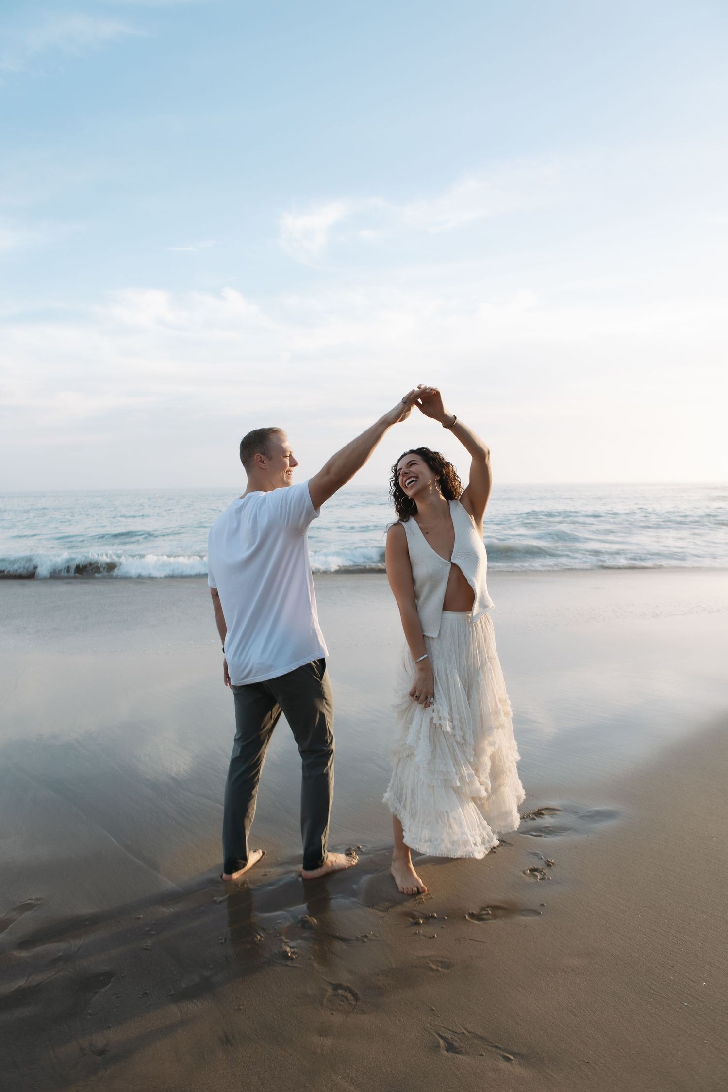 A couple dances together on a misty beach at sunset, creating footprints in the wet sand.