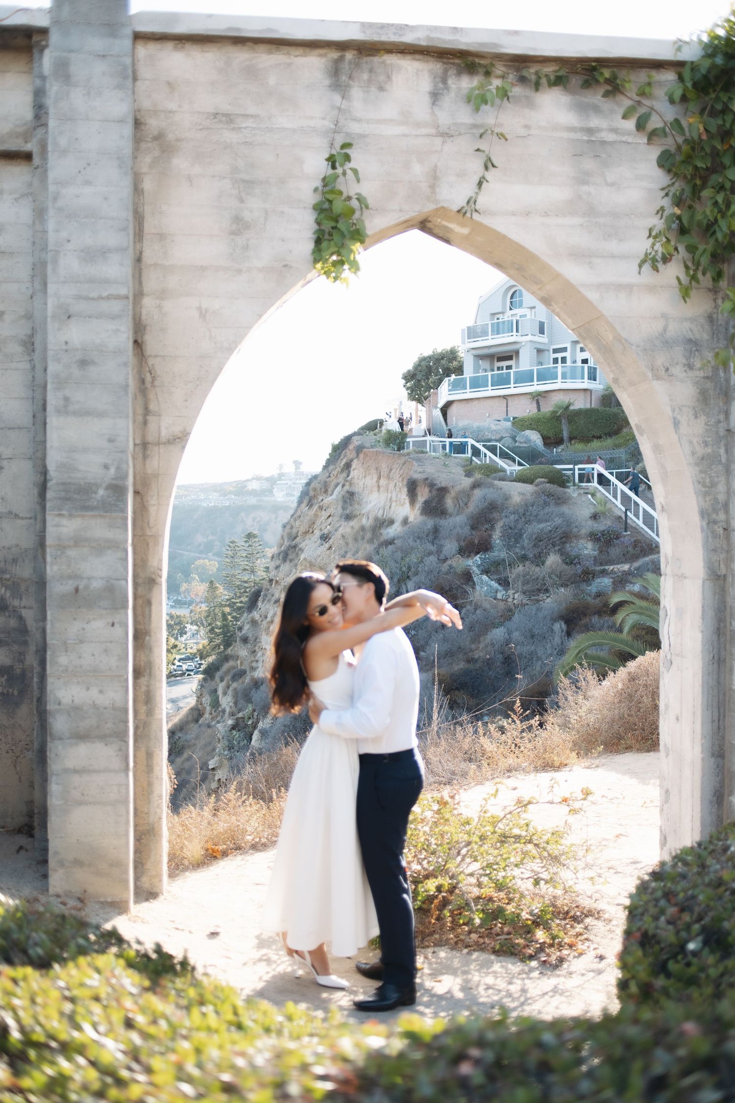 A romantic wedding moment captured under concrete bridge arches with scenic mountain views in the background.