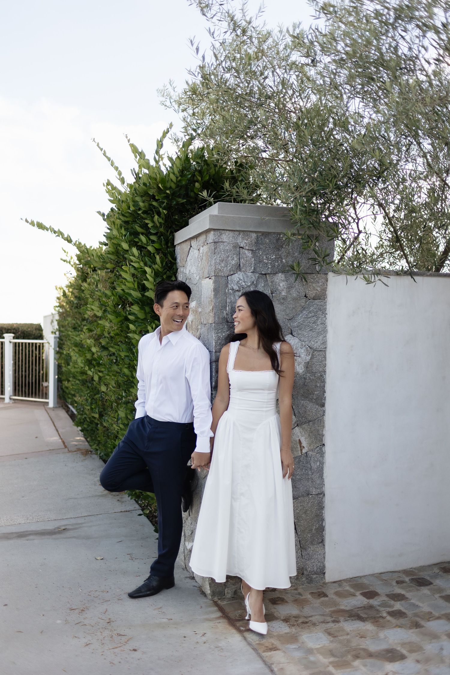 A couple in white and navy attire shares romantic moments against a stone wall in a series of outdoor photos.