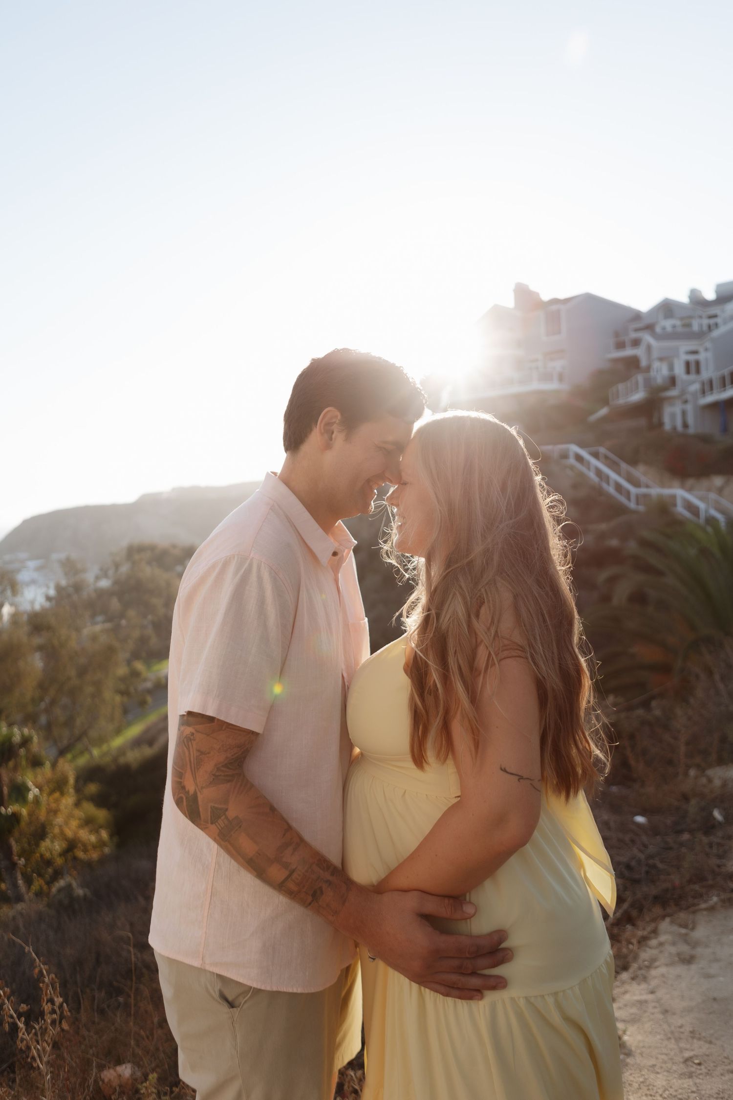 A couple embraces in golden sunlight on a hillside during a romantic sunset photoshoot.