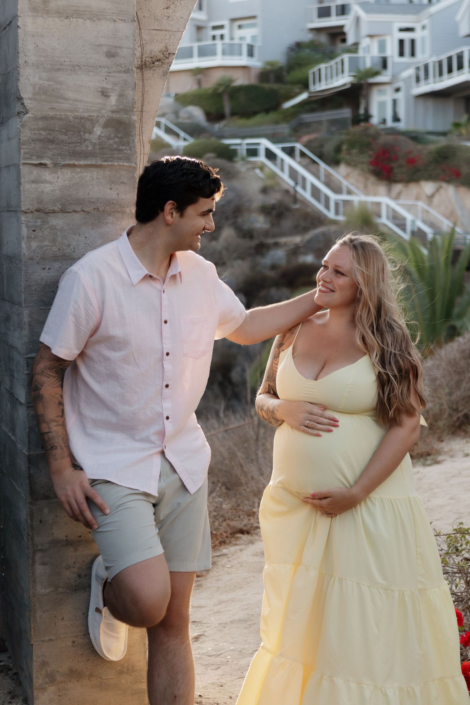 A couple shares romantic moments on a beach at sunset wearing yellow and white outfits.