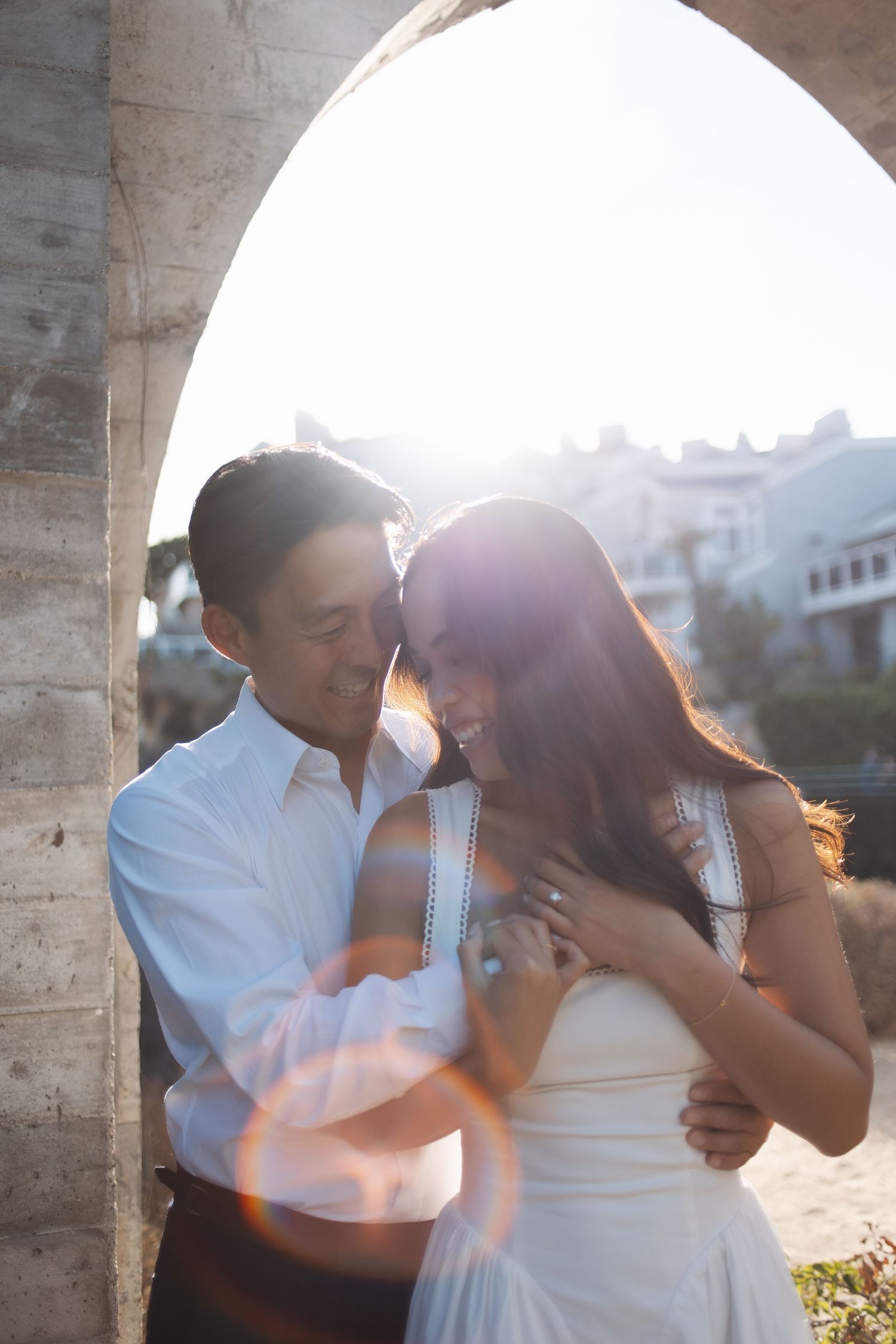 A romantic couple embraces and dances together at sunset under concrete archways.