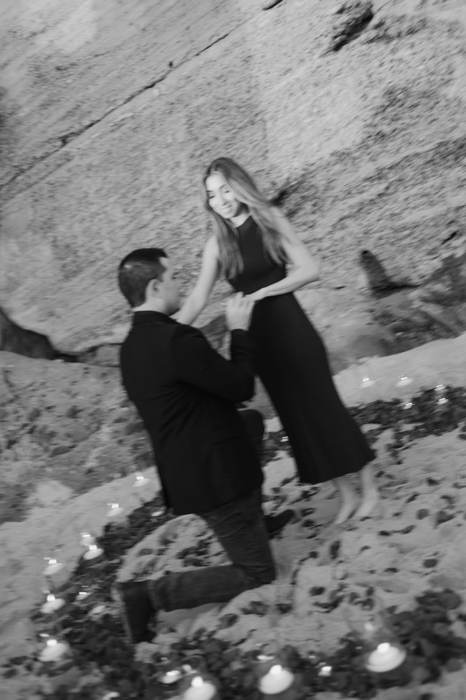 A romantic black and white proposal moment captured on rocky terrain with candles scattered around the couple.