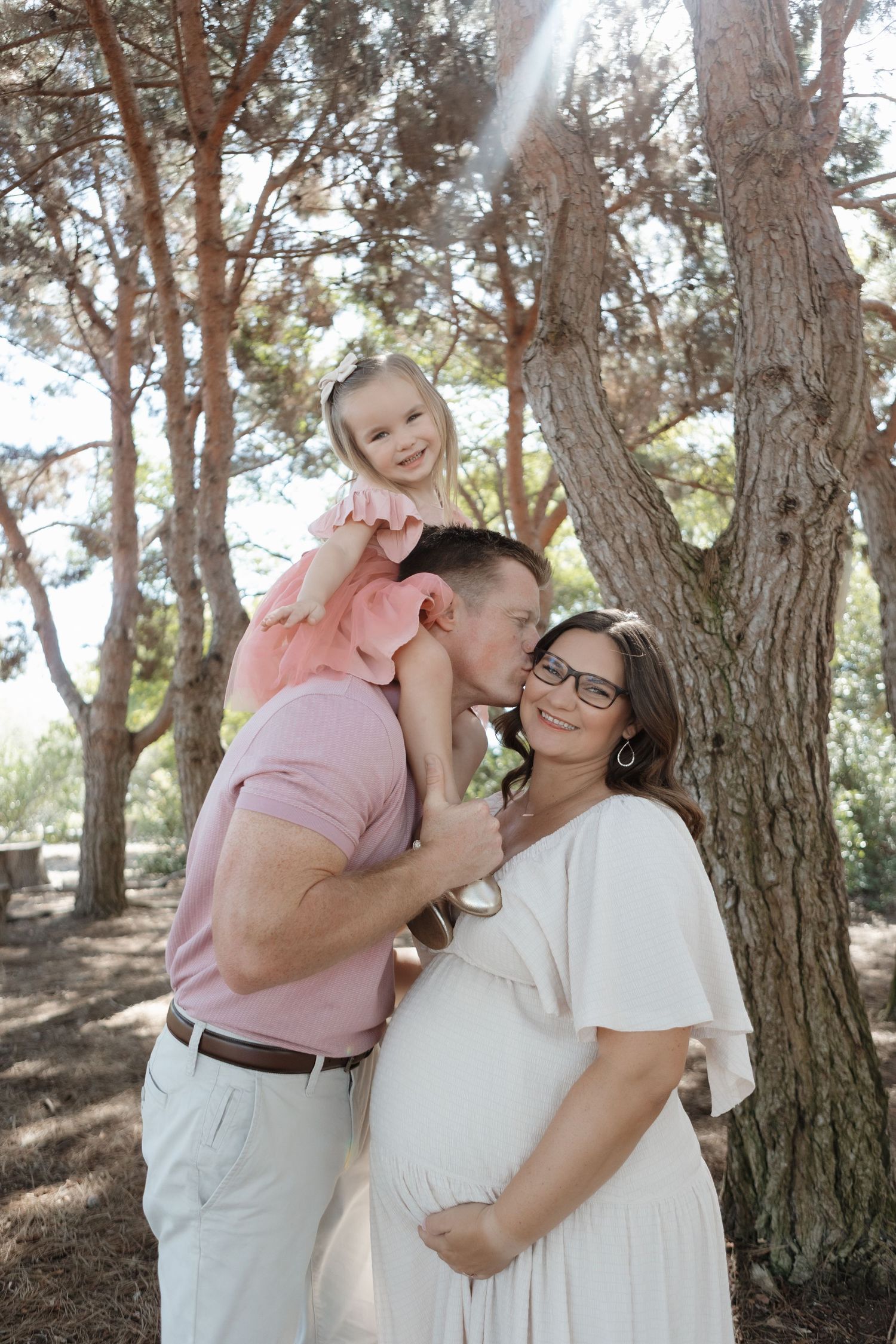 A romantic couple shares tender moments among tall pine trees in a forest setting during a photo session.