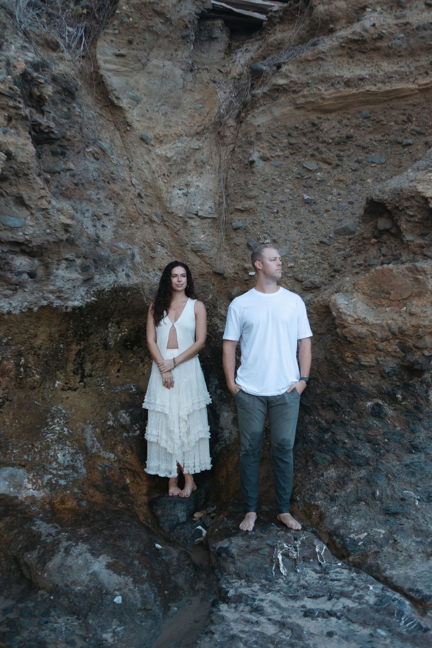 Couple poses against rugged rock face in artistic engagement photo series.