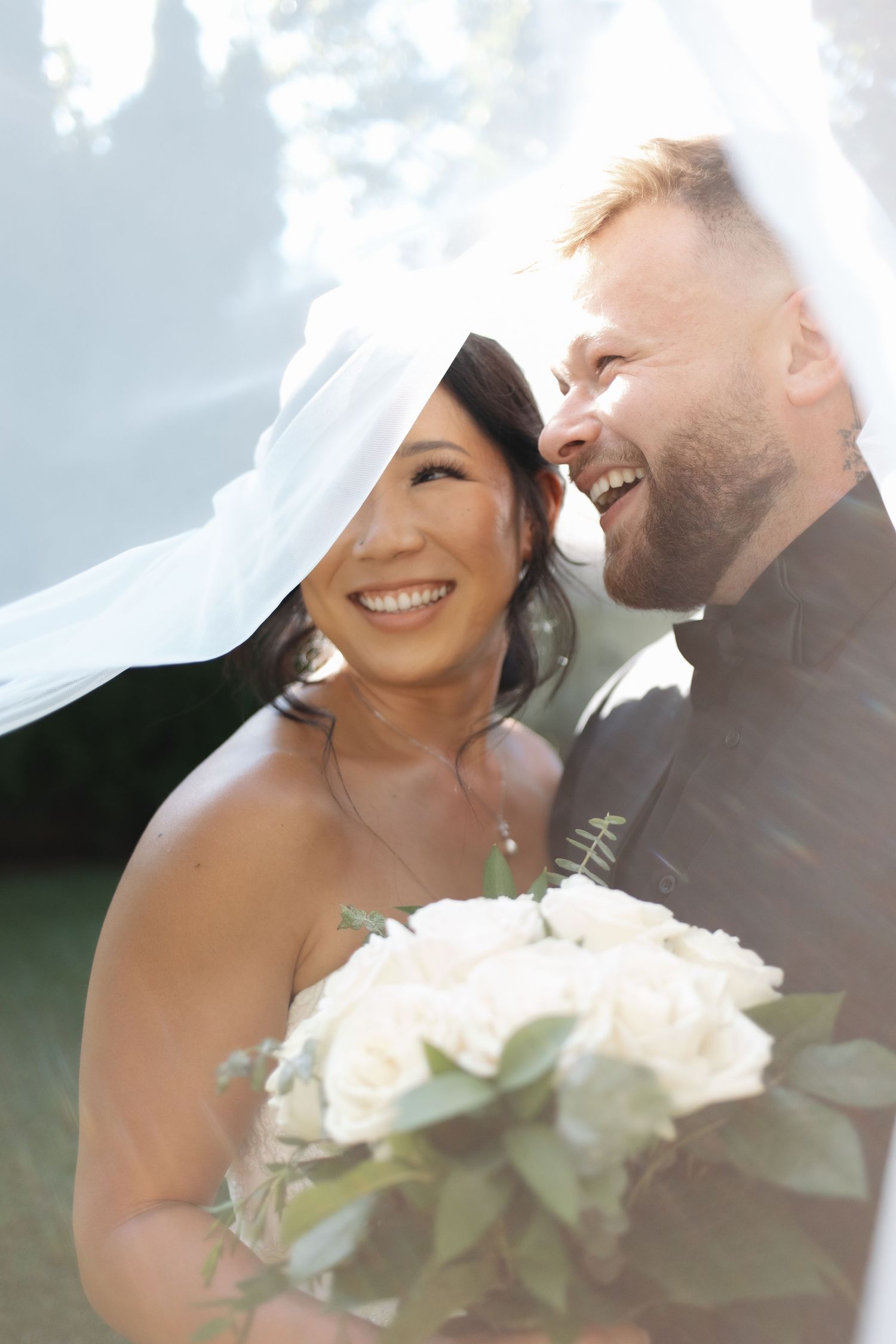 A joyful wedding moment captured in bright sunlight with white bouquet.