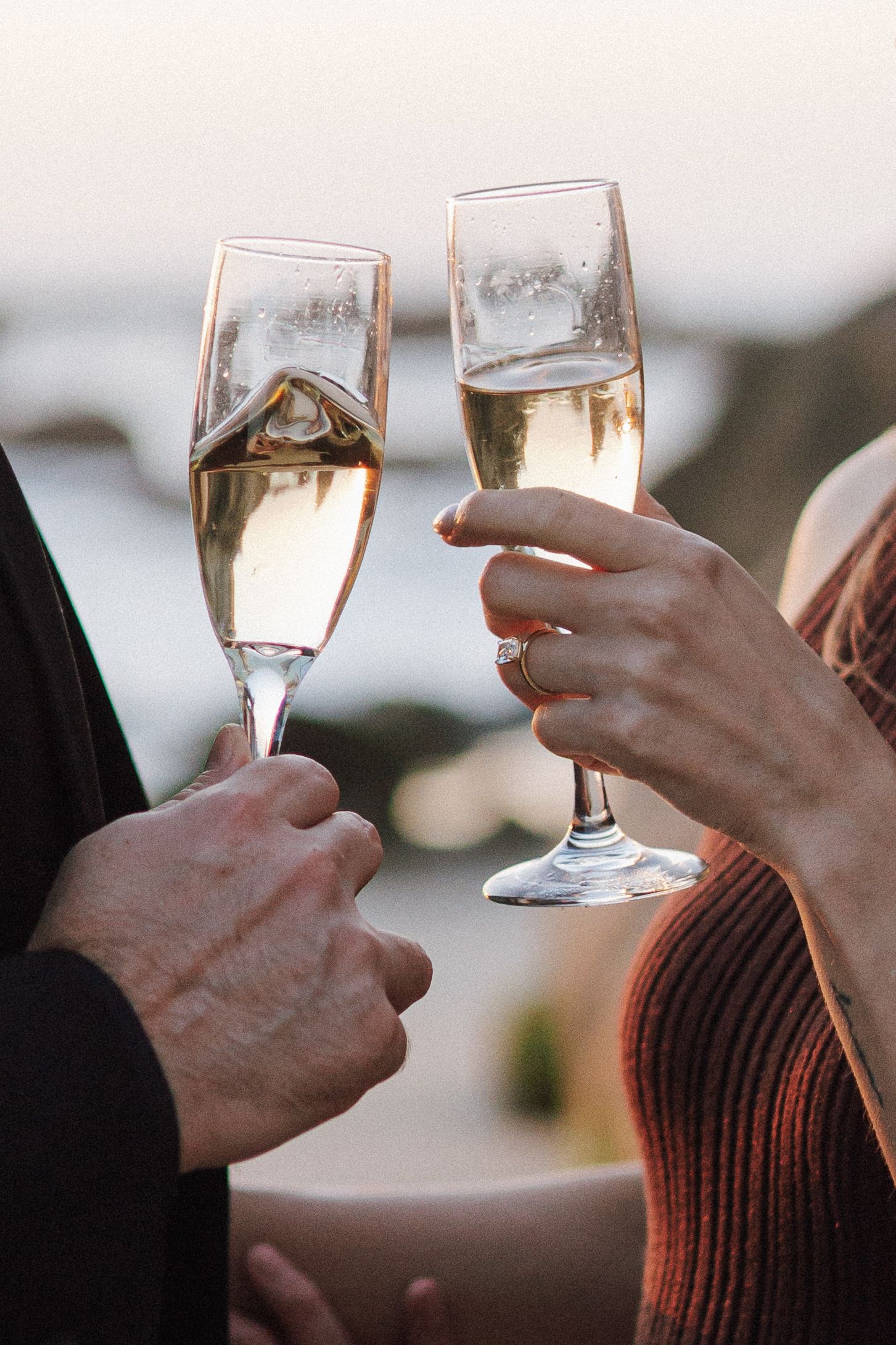 Two hands toasting with champagne flutes filled with sparkling wine against a blurred background.