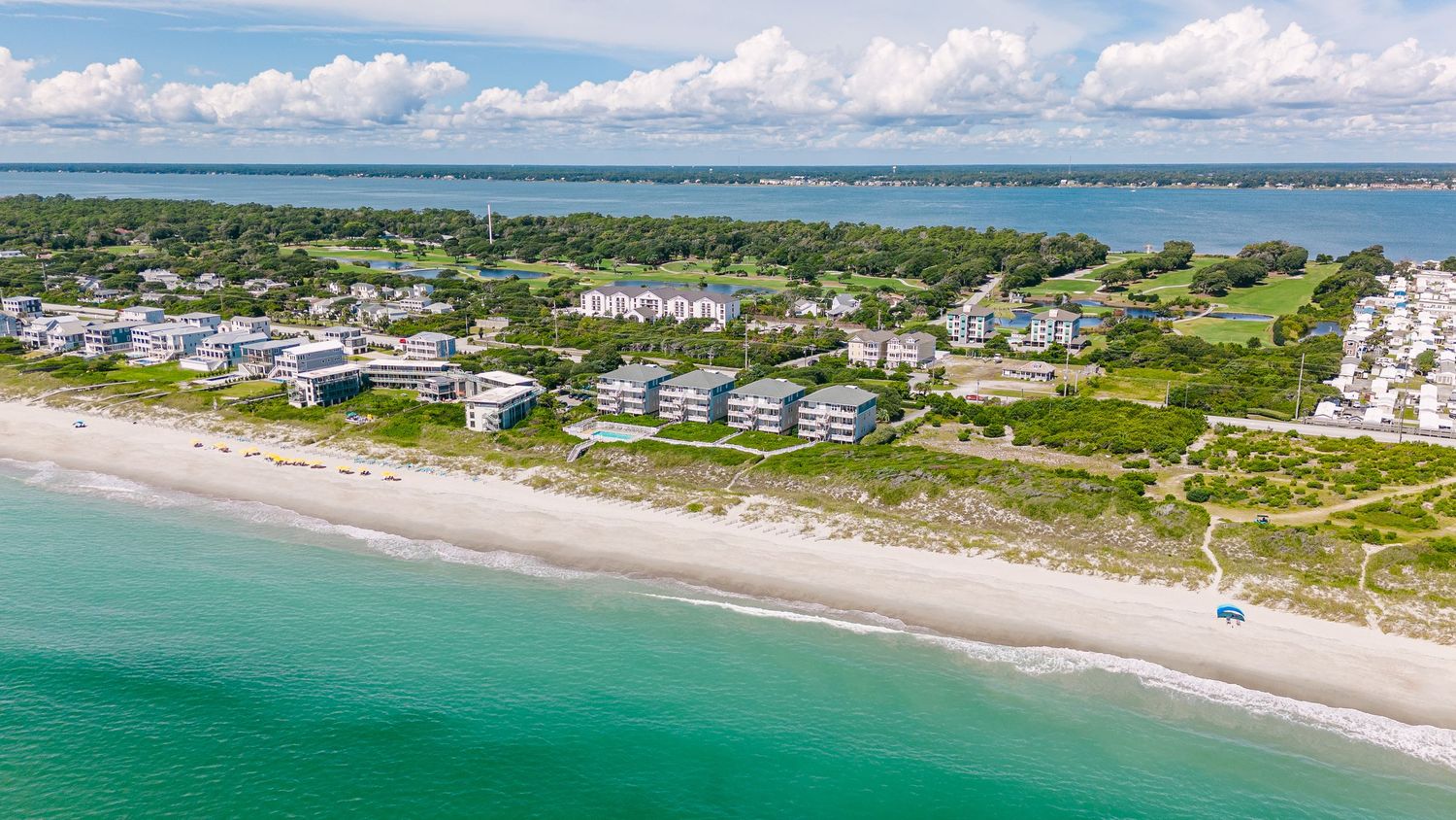 Aerial view of beachfront condominiums along a pristine turquoise coastline with lush greenery.