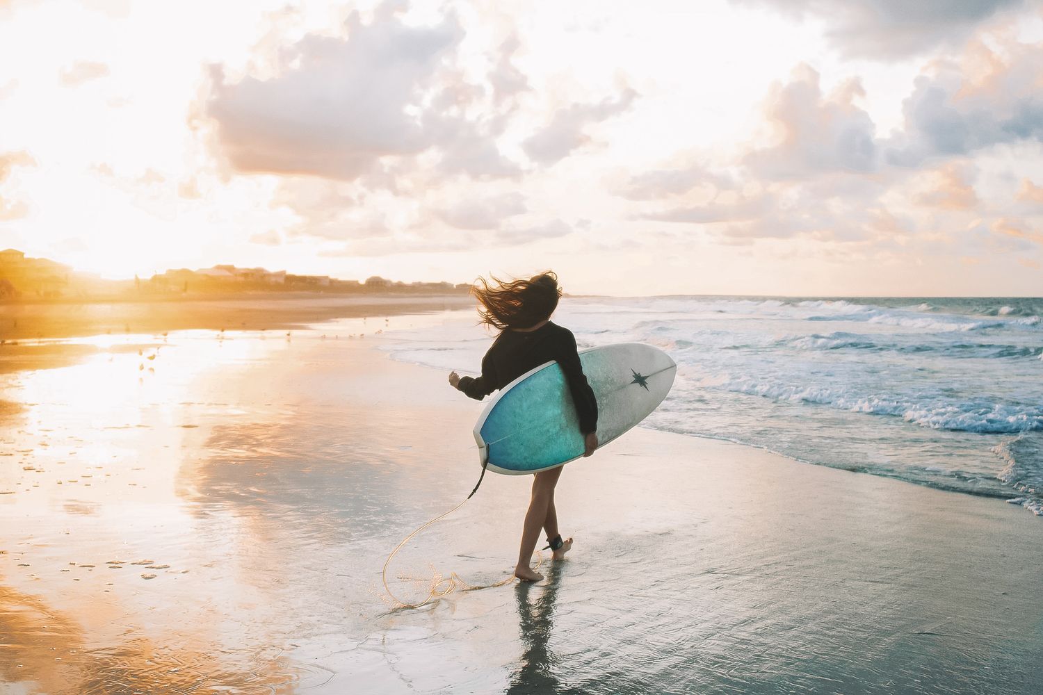 Surfer carrying board on beach at golden sunset.