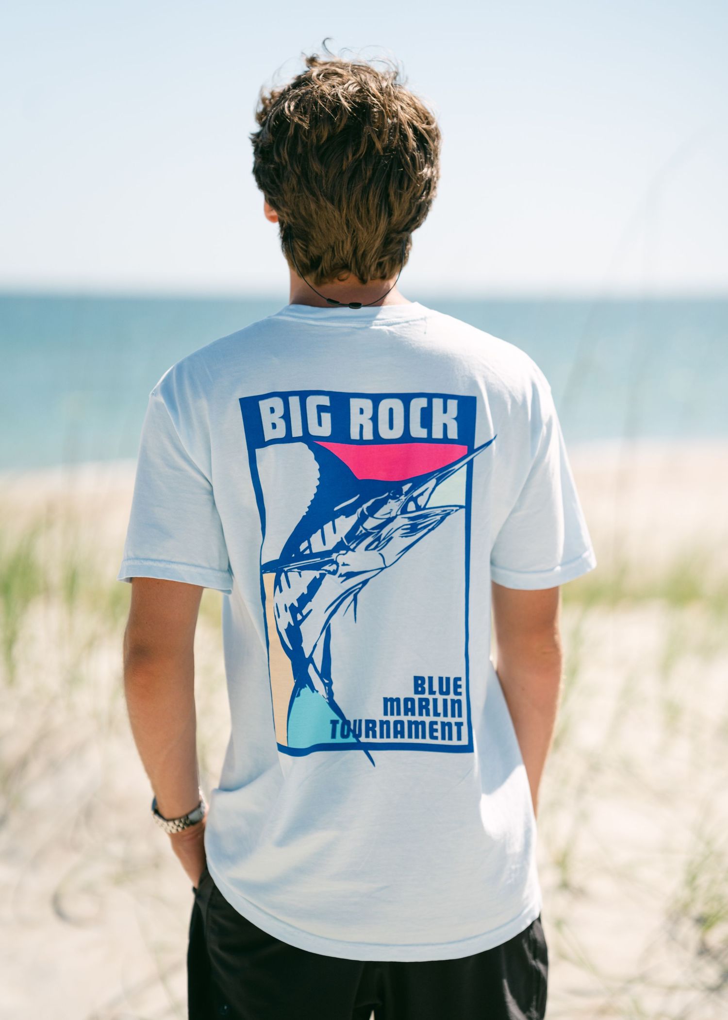 Man wearing a Big Rock Blue Marlin Tournament graphic tee on a beach.