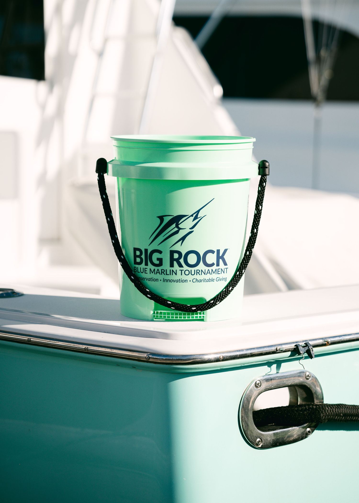 Green Big Rock Blue Marlin Tournament bucket with rope handle sits on the edge of a boat at the marina.