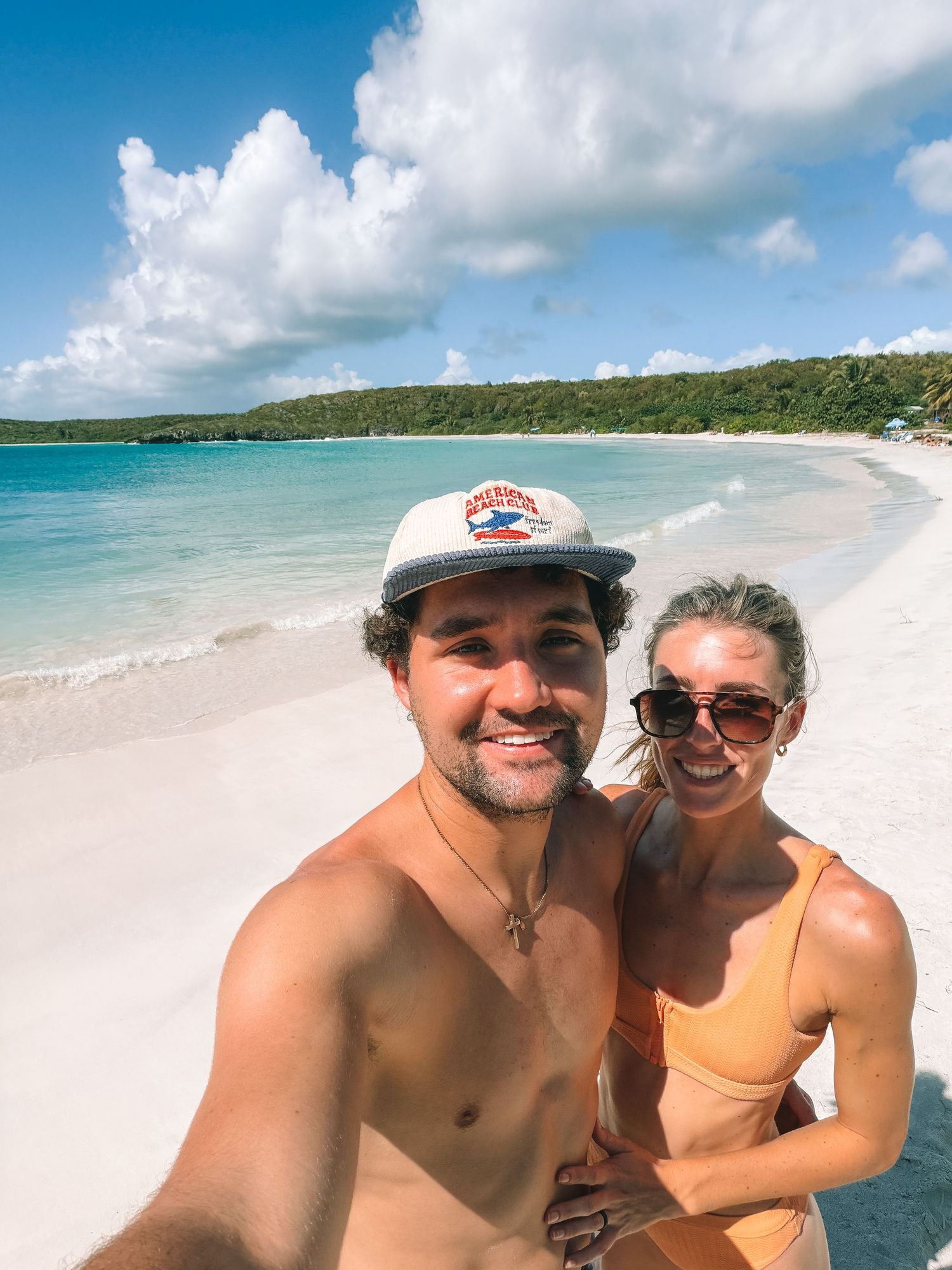 Smiling couple taking beach selfie with turquoise water and white sand beach in tropical destination.