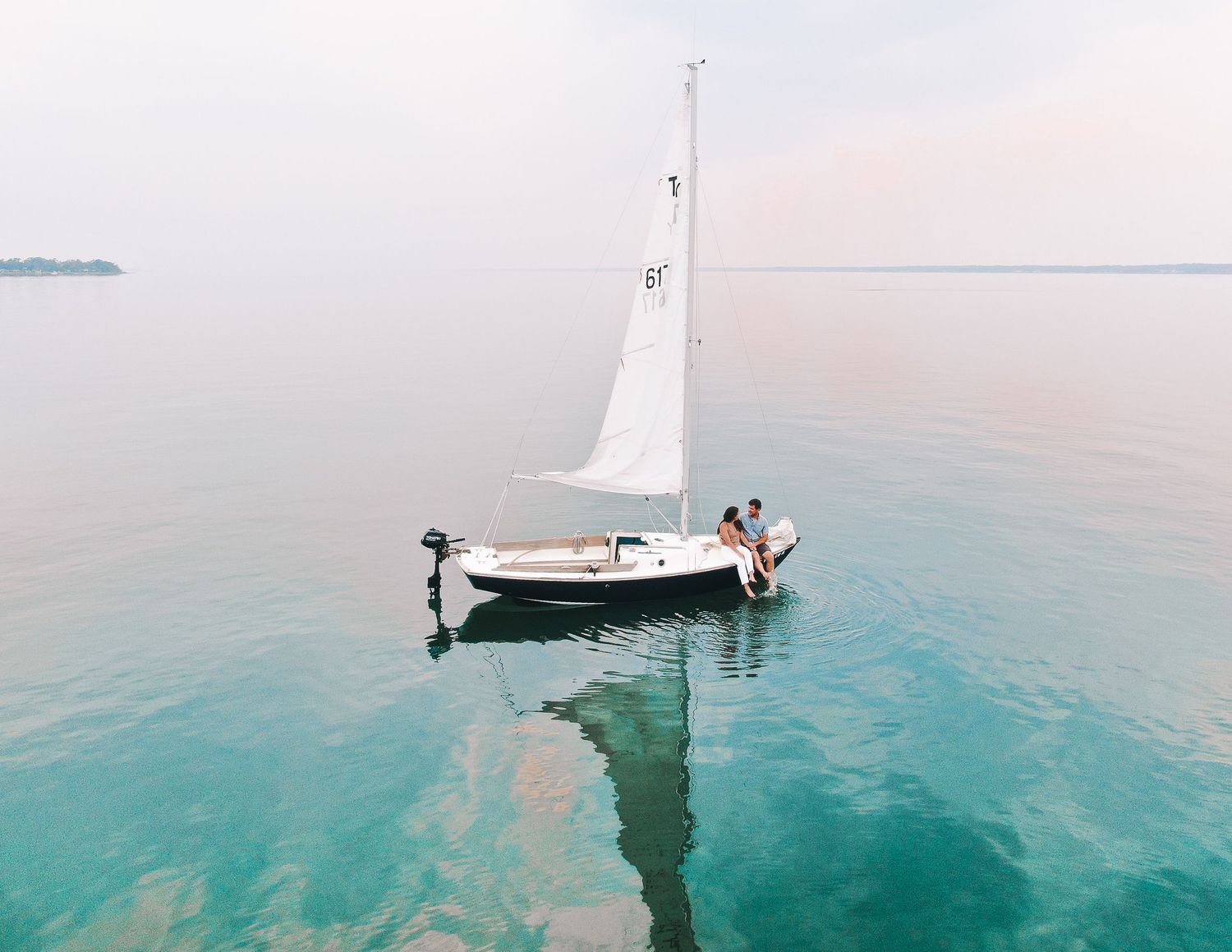 Drone shot of white sailboat with couple aboard on serene turquoise lake.