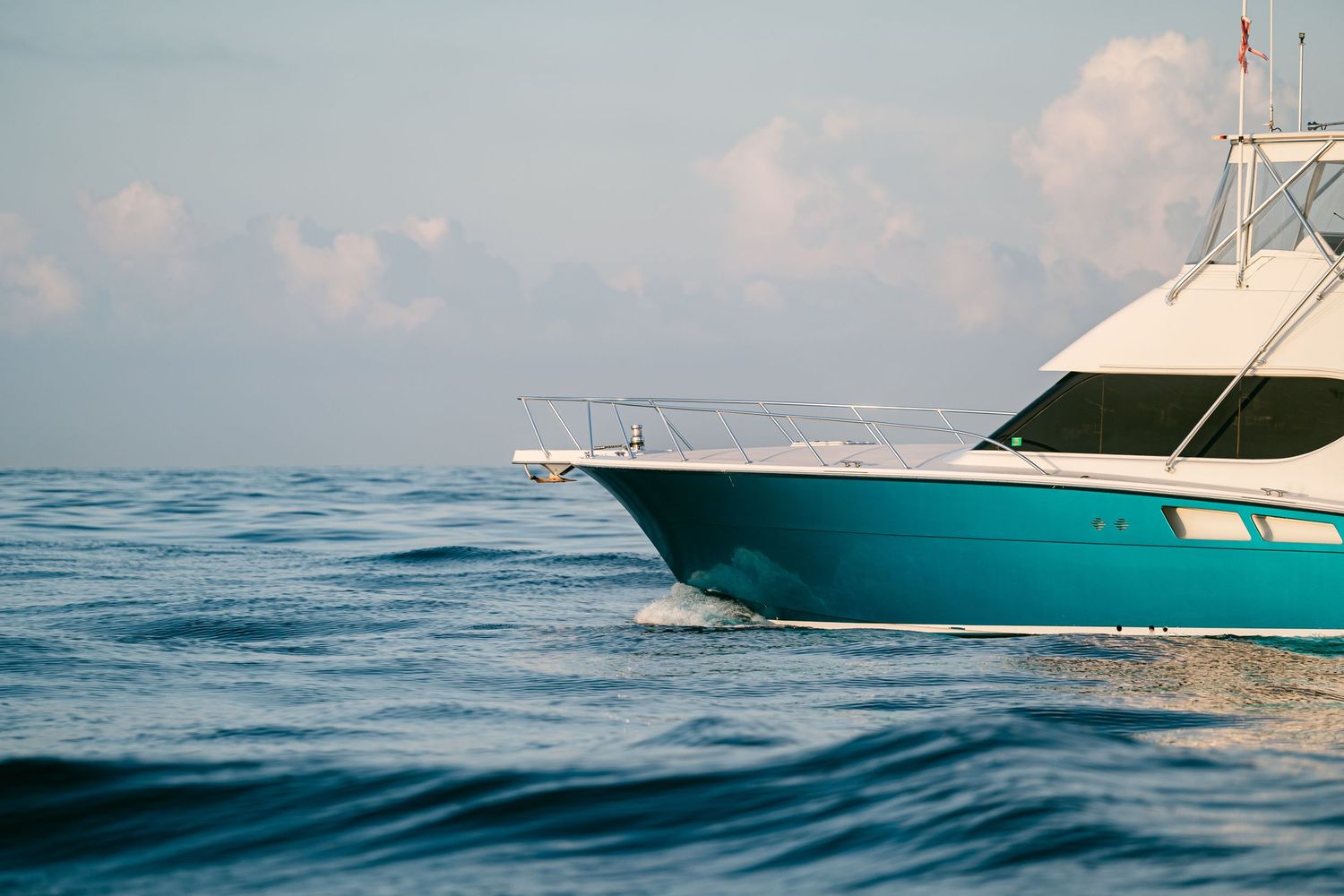 Turquoise and white sport fishing boat sailing on calm blue ocean waters under cloudy sky.