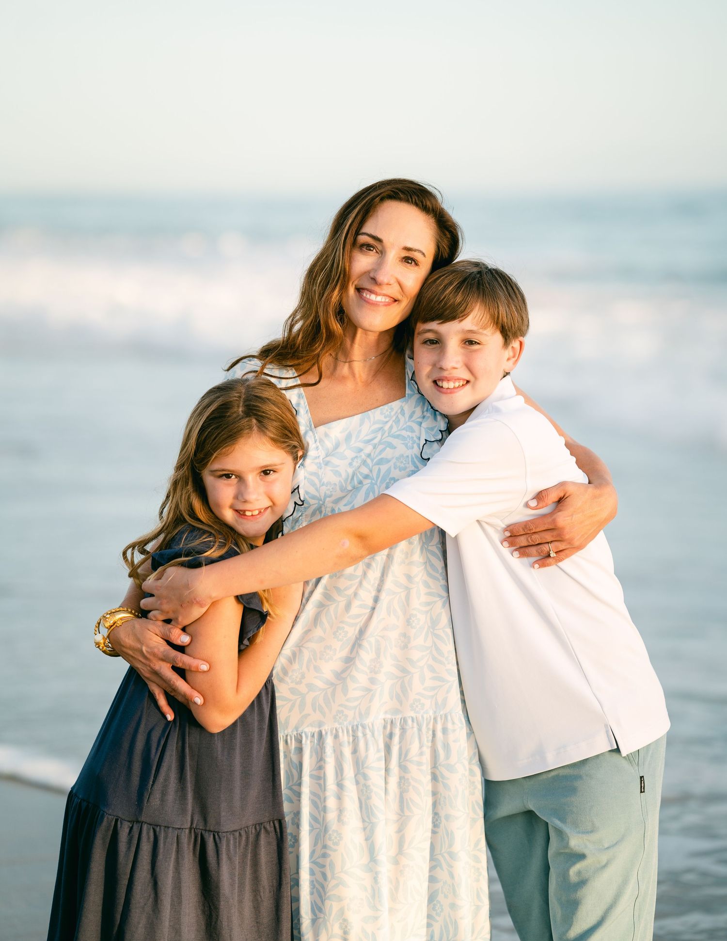 Mother hugging her two children on a sunny beach shoreline.