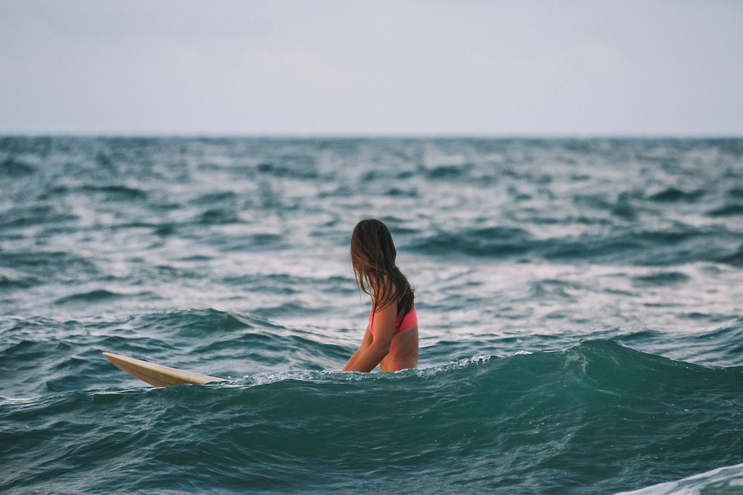 Woman in red bikini sitting on surfboard in ocean waves.