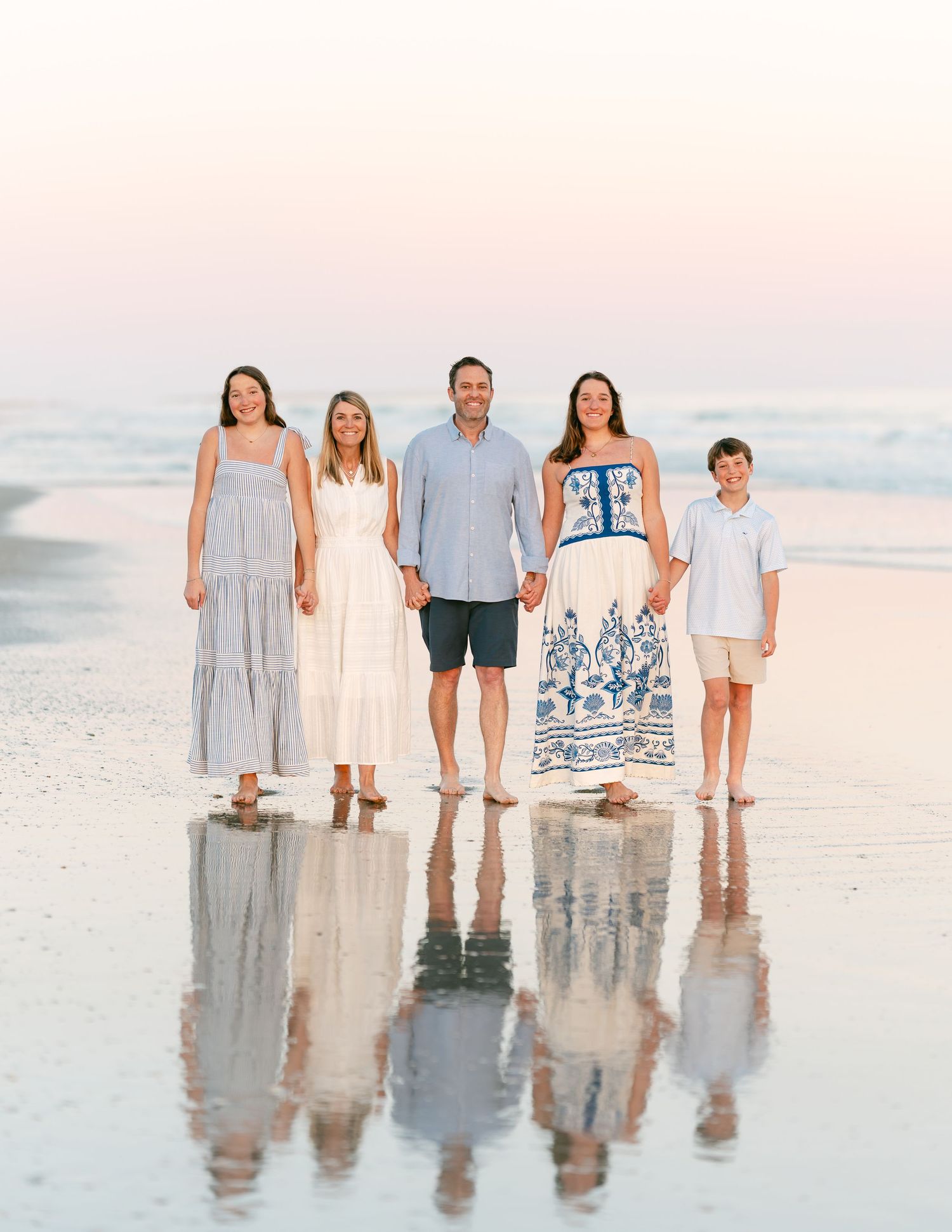 Happy family of five posing together on a calm reflective beach during golden hour.