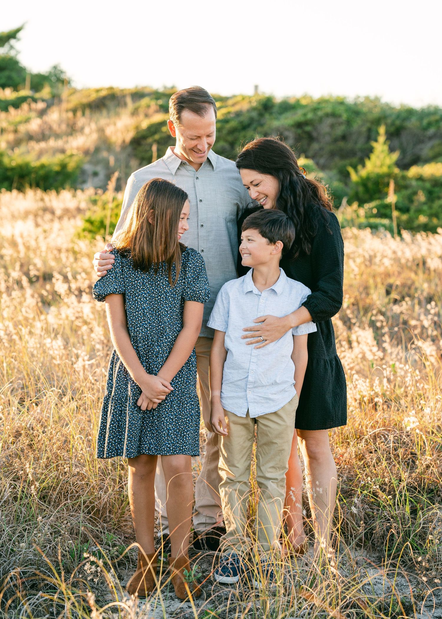 Family of four sharing a warm embrace in a golden field at sunset.
