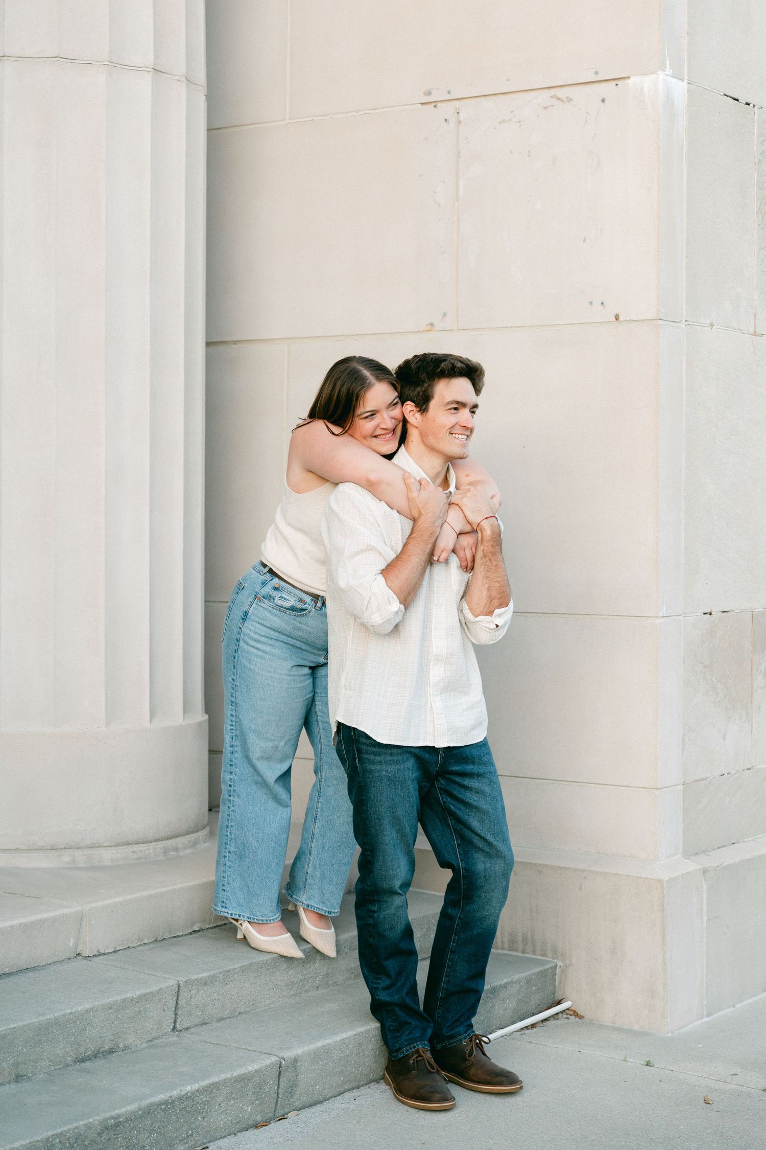 Happy couple embracing on stone steps beside white columns in a bright outdoor setting.