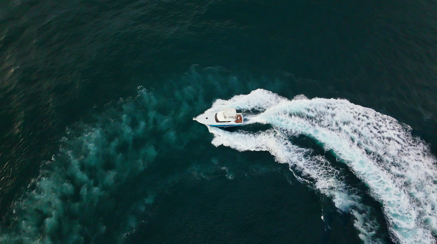 Aerial view of a white sport fishing boat cutting through deep turquoise ocean water leaving a white wake.