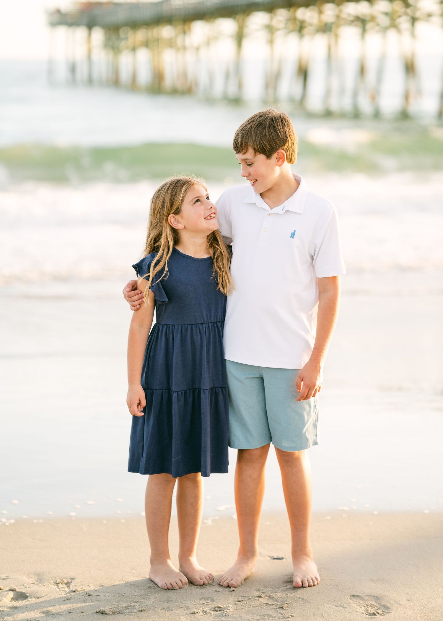 Young boy and girl siblings smiling together on beach by pier.