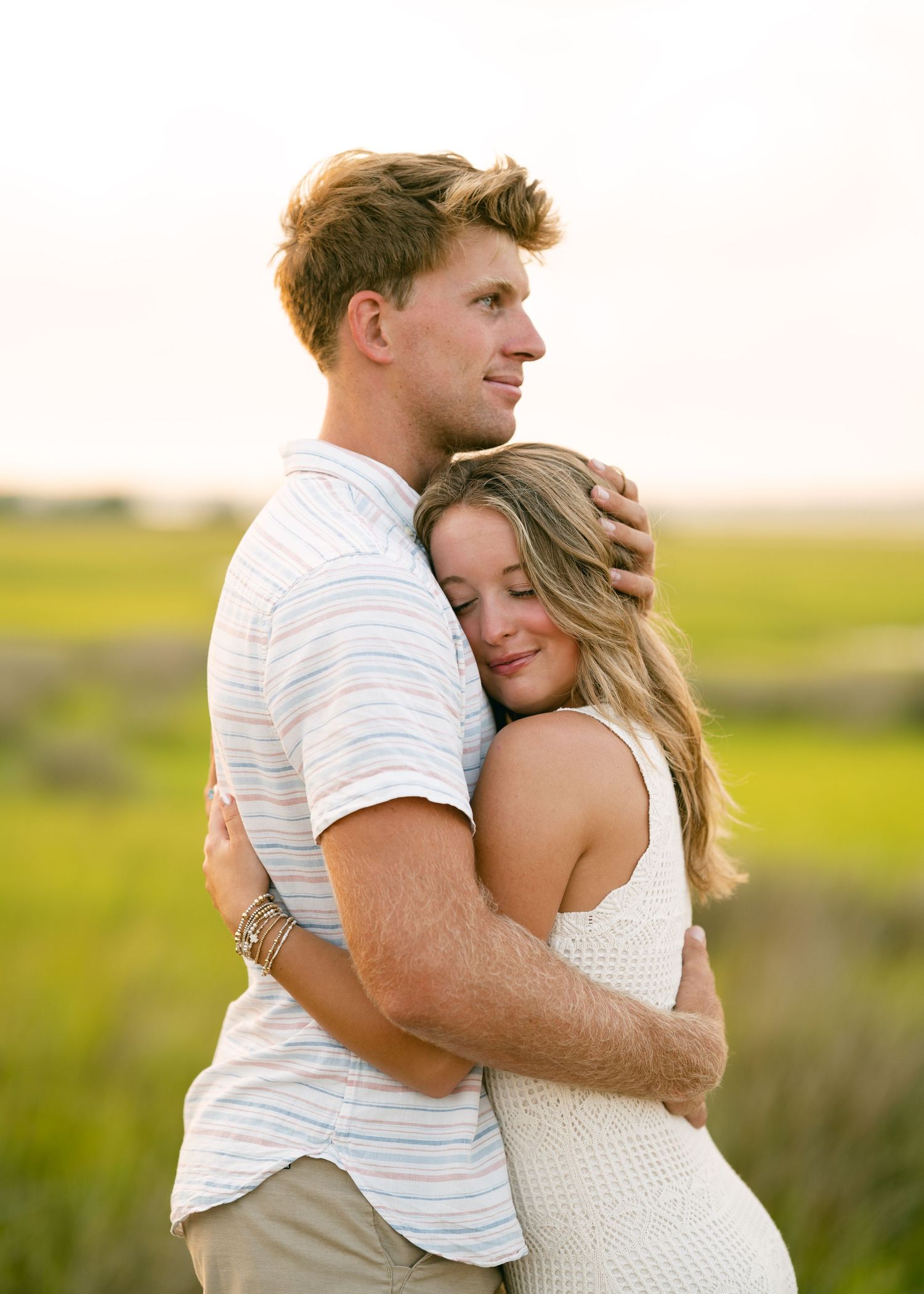Young couple embracing in a golden field at sunset during an outdoor engagement photo session.