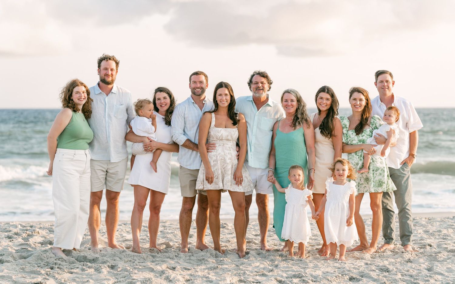 Large extended family posing together on a sandy beach at sunset.