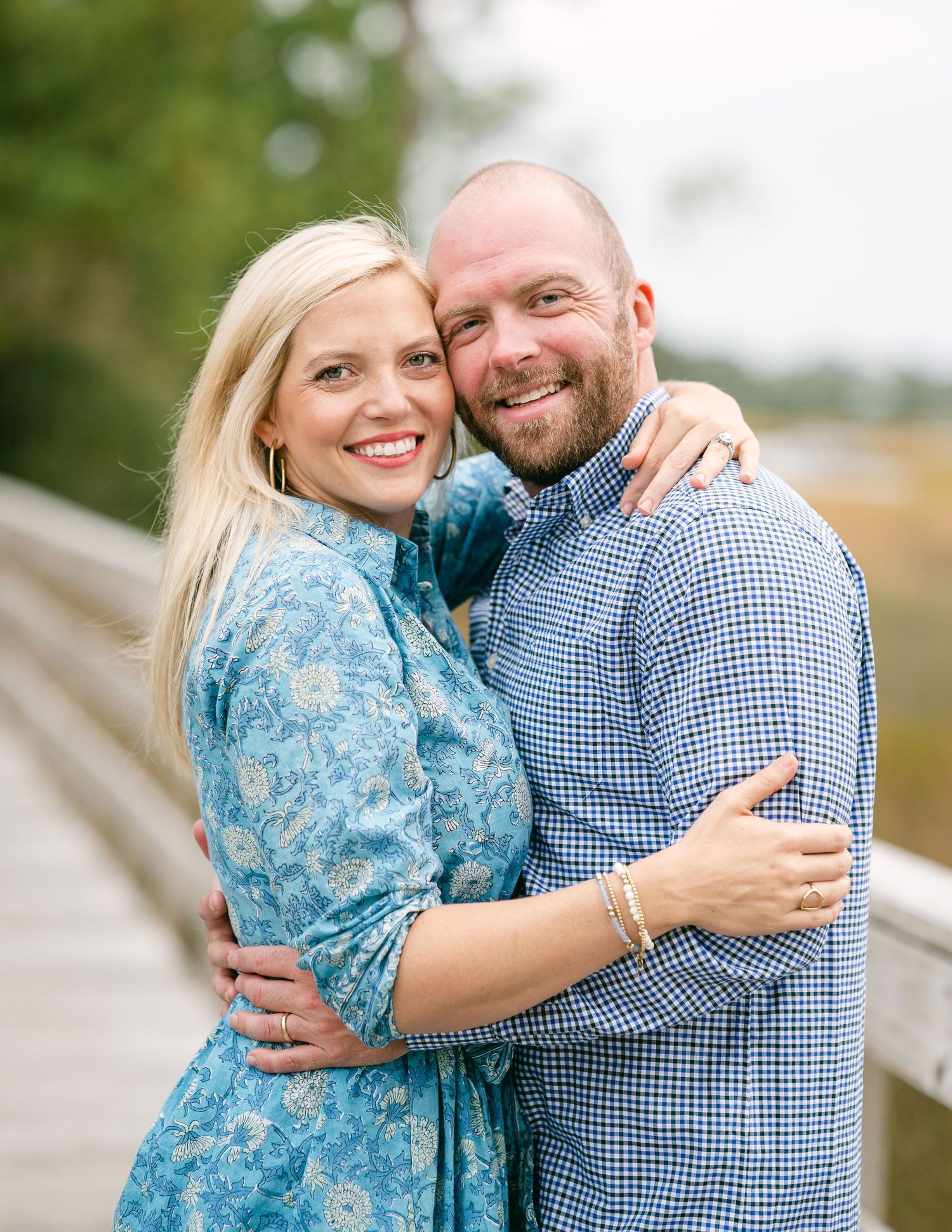 Blonde woman and bearded man smiling and embracing on a wooden bridge for engagement photos.