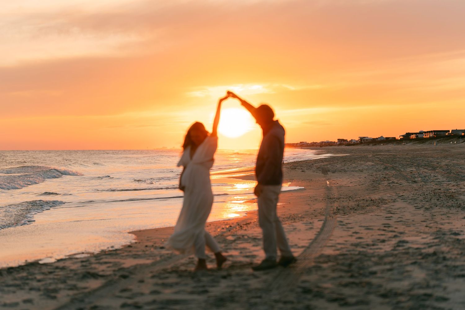 Couple dancing joyfully on the beach silhouetted against a vibrant orange sunset sky.