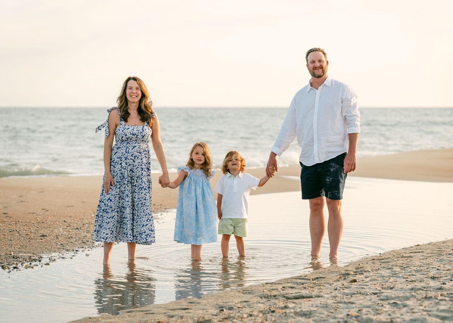 Happy family of four holding hands walking along a sandy beach at golden hour.