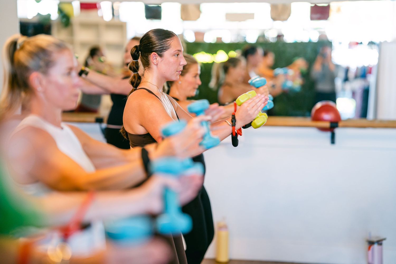 Women exercising with colorful dumbbells at barre fitness class.