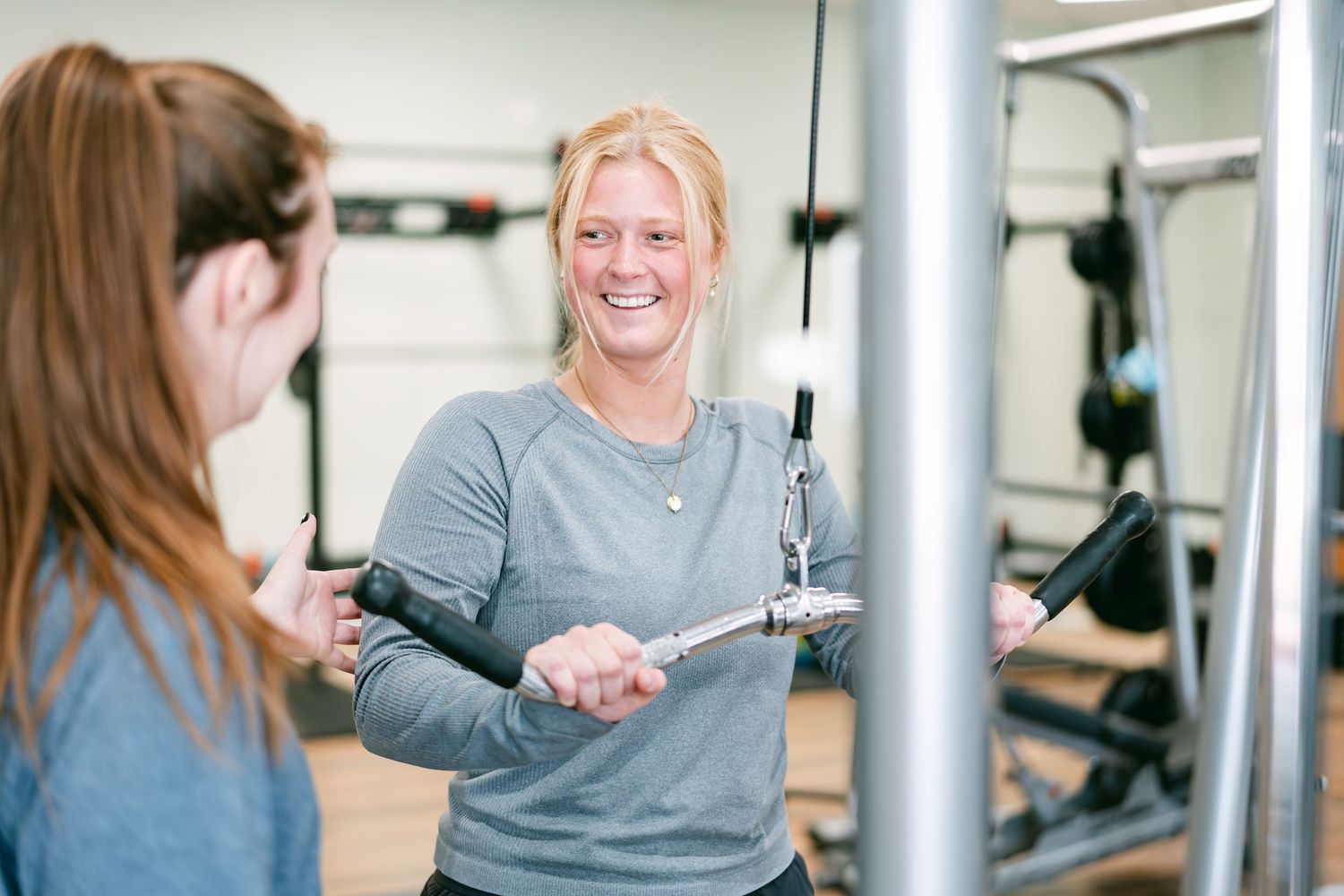Woman smiling while using cable machine at gym during personal training session.