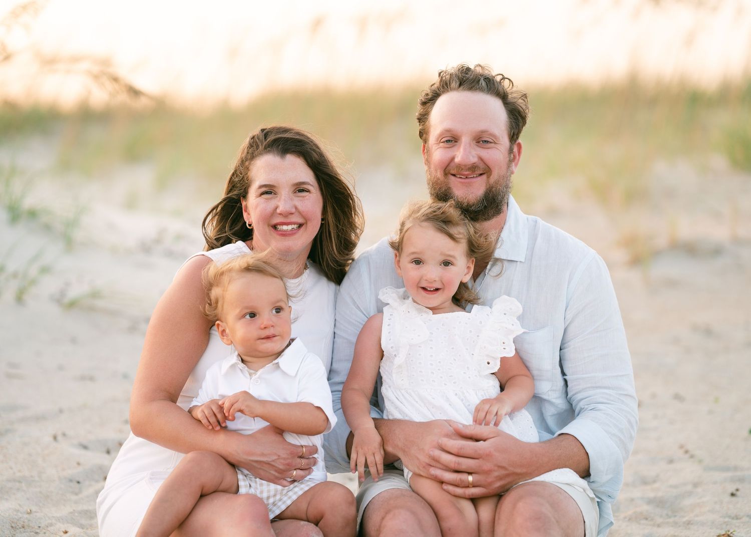 Happy family of four with two toddlers sitting together on a sunny beach.