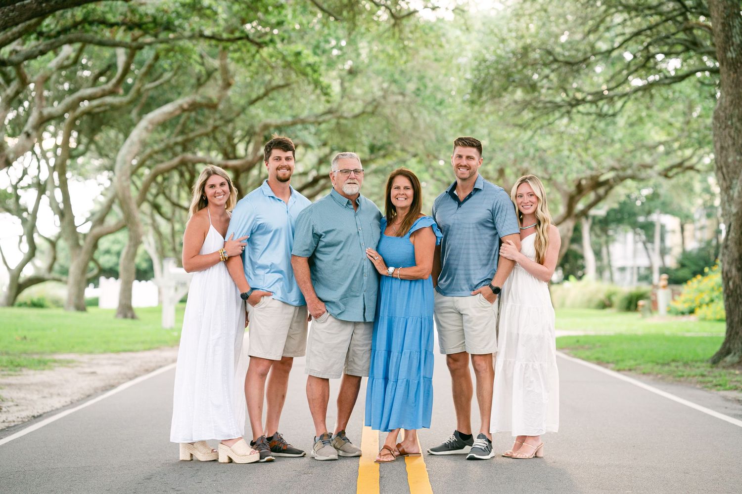 Family of six posing on tree-lined road in coordinating blue and white outfits.