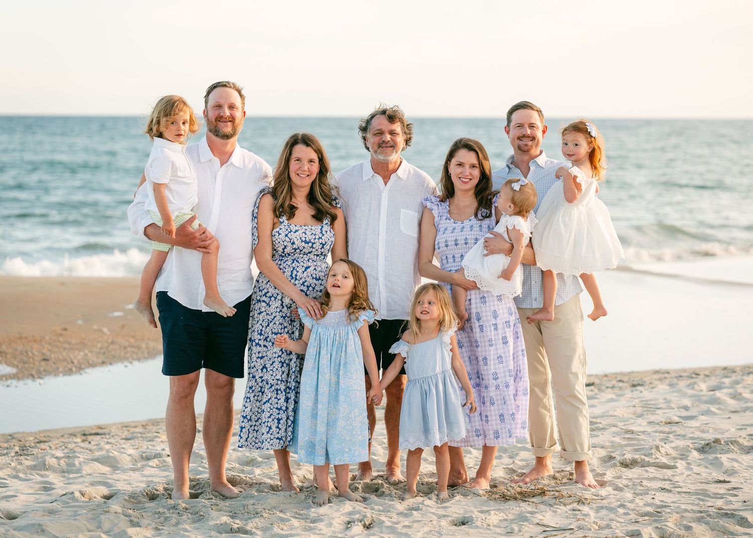 Large extended family with young children smiling together on sunny beach.