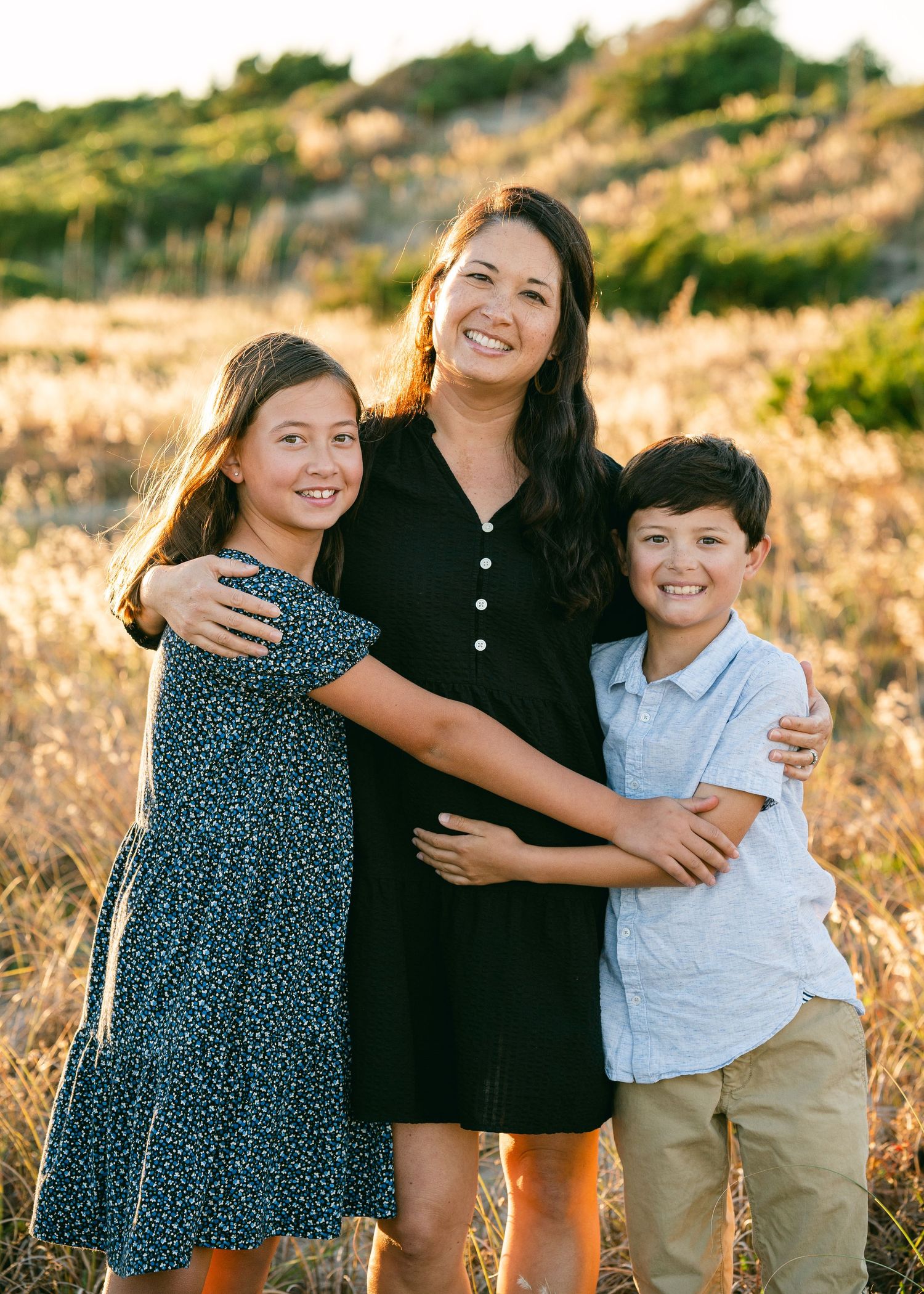 Smiling mother hugging her two children outdoors in a sunny field.
