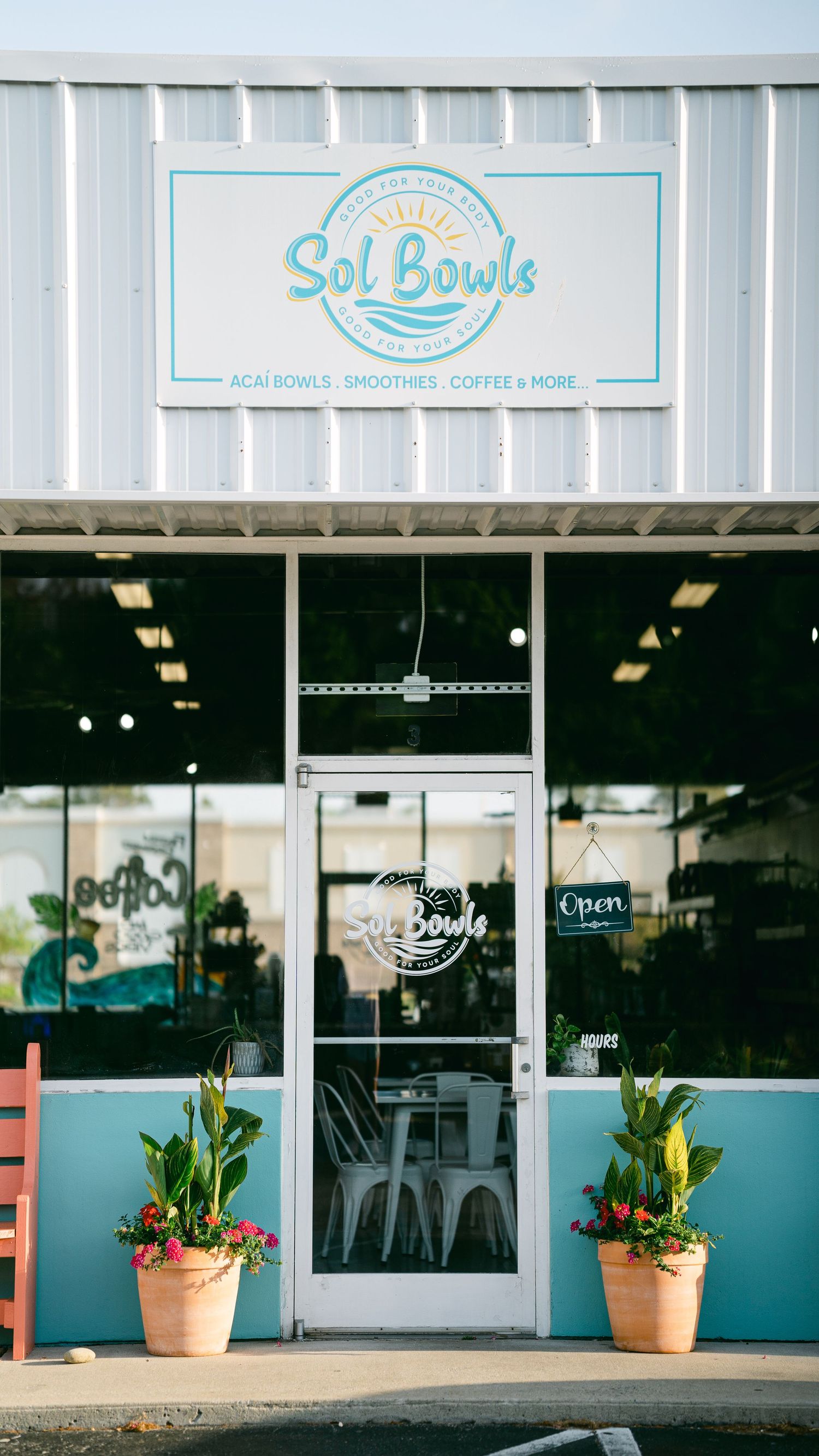 Exterior of Sol Bowls cafe featuring teal accents, large windows, and potted tropical plants at entrance.