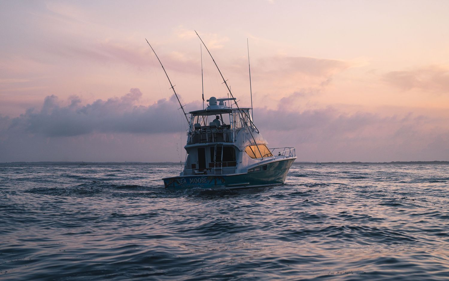 Sport fishing boat with tall rods silhouetted against a dramatic pink and purple sunset sky.